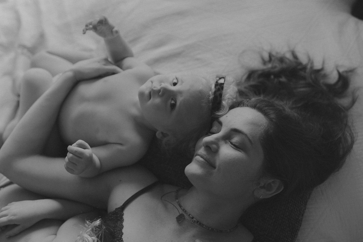 Black and white photo of a mother and baby lying together on a bed, sharing a peaceful bonding moment.