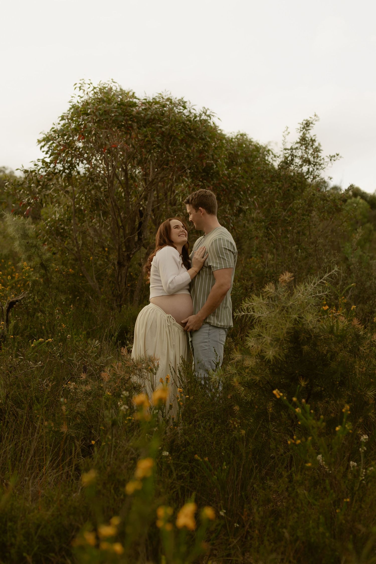 Couple embracing in a wildflower meadow, pregnant woman in white dress, romantic outdoor maternity photo session.