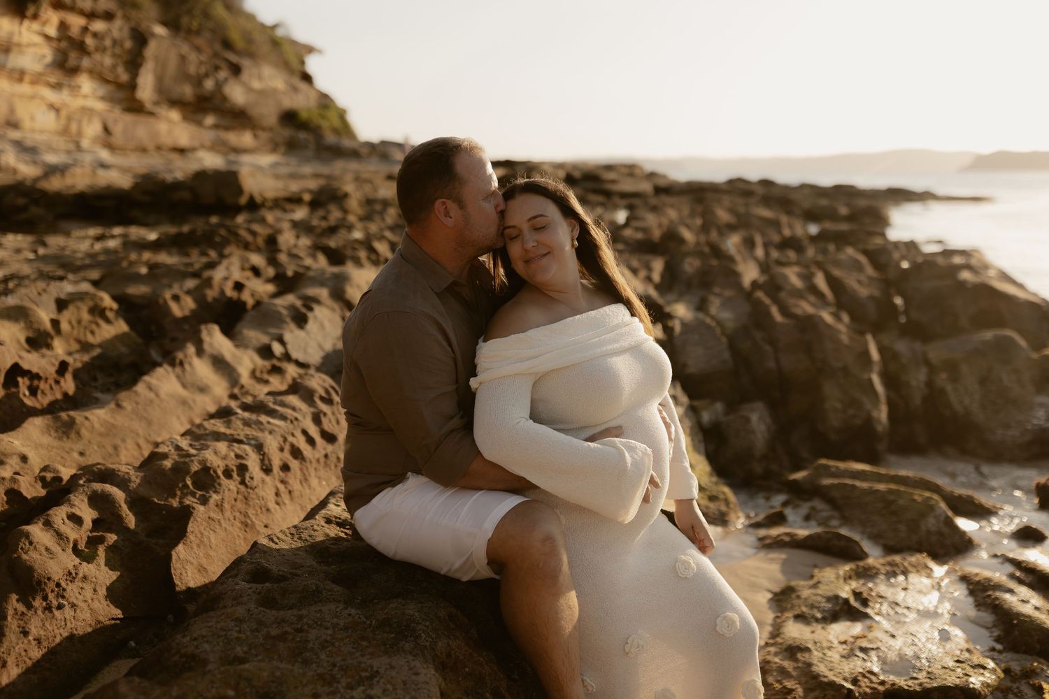 Romantic couple shares intimate moment on rugged oceanside cliffs at sunset.