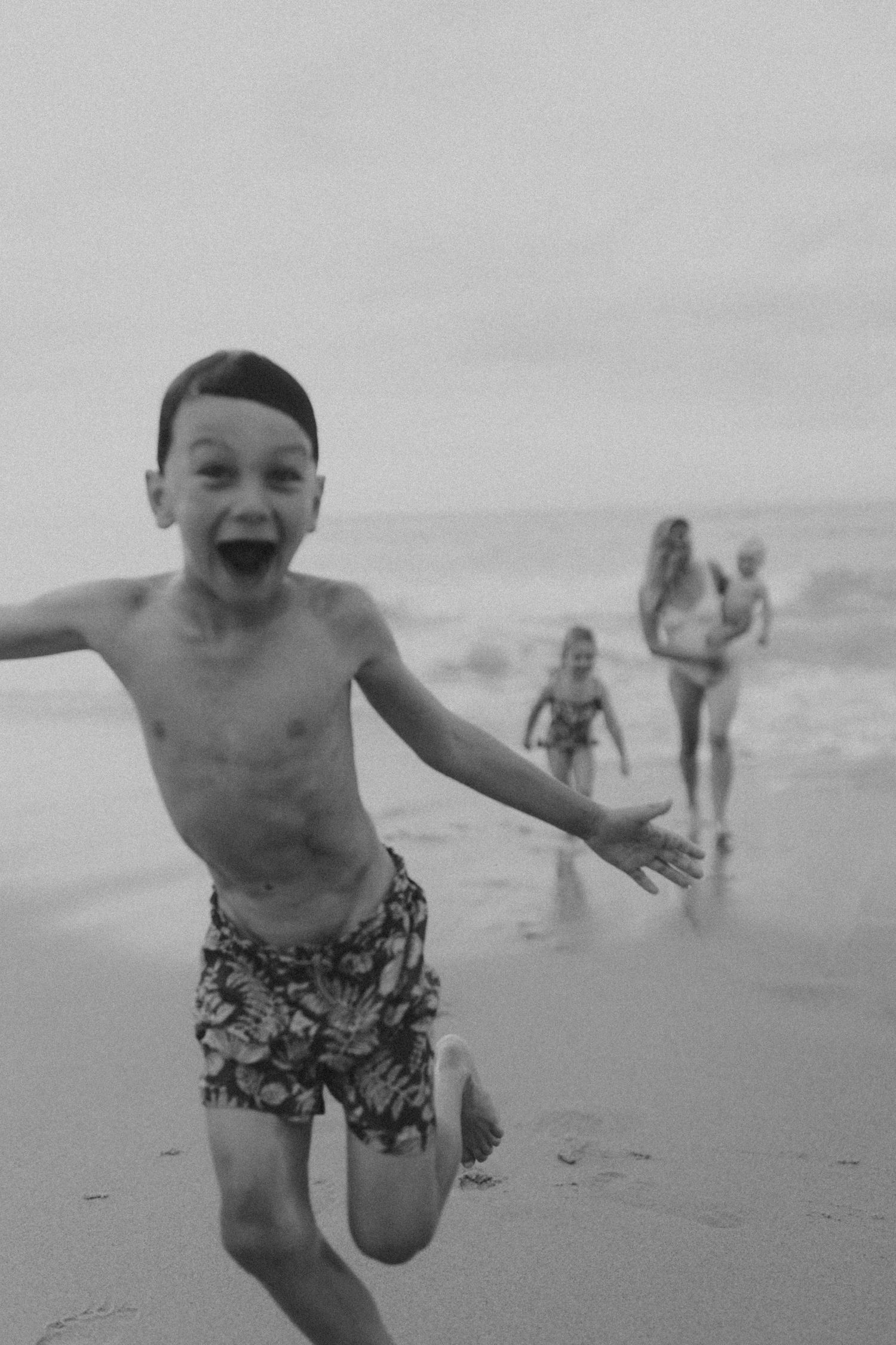 Young child running and playing joyfully on a beach in black and white.