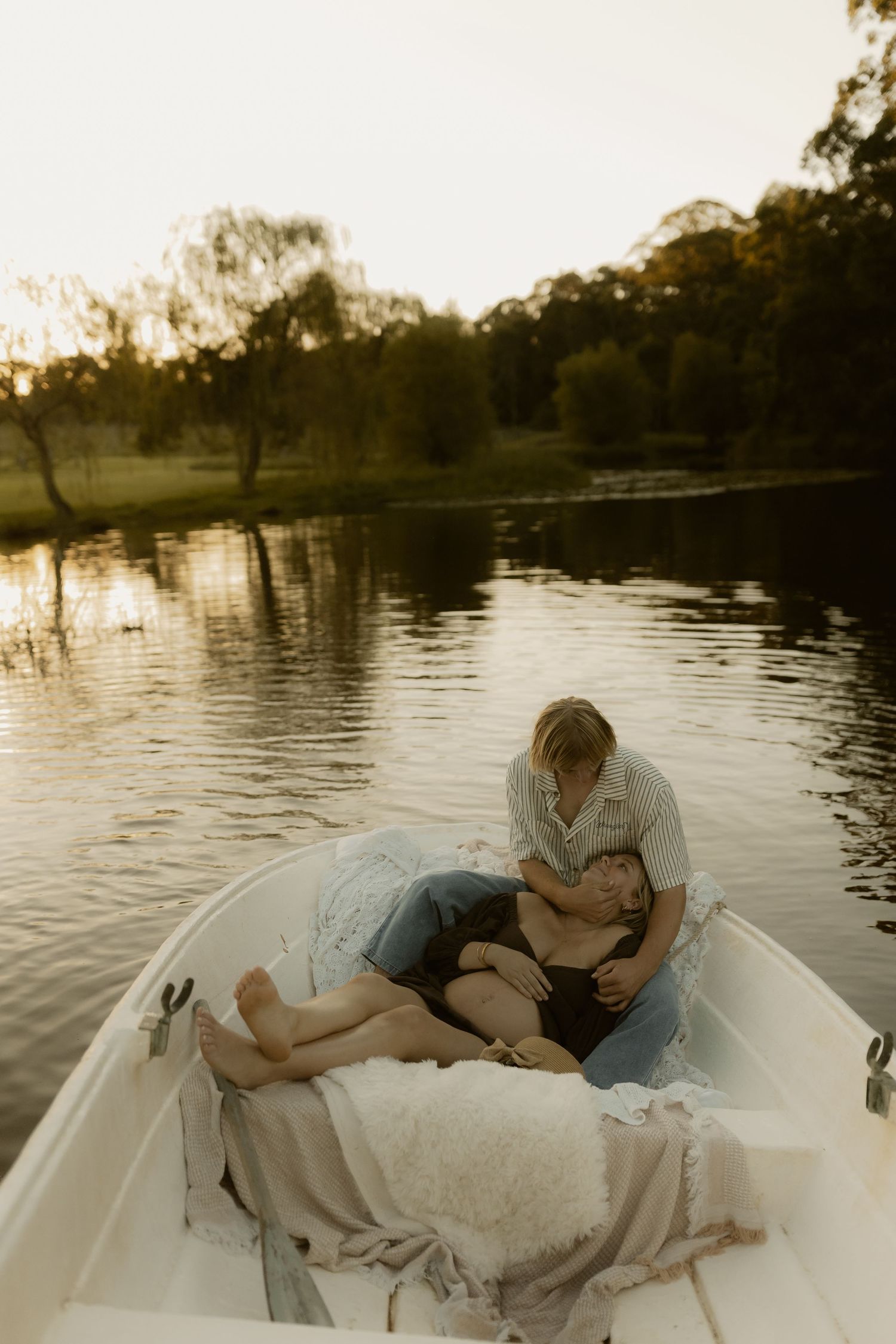 Couple relaxing together in a white boat on a serene lake at dusk.