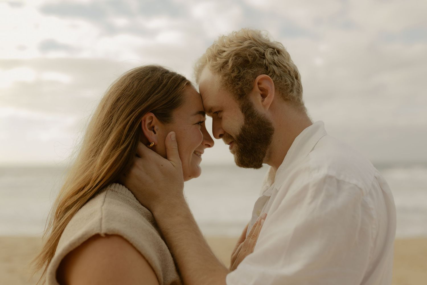 A tender moment between a couple on the beach with soft lighting and natural scenery.