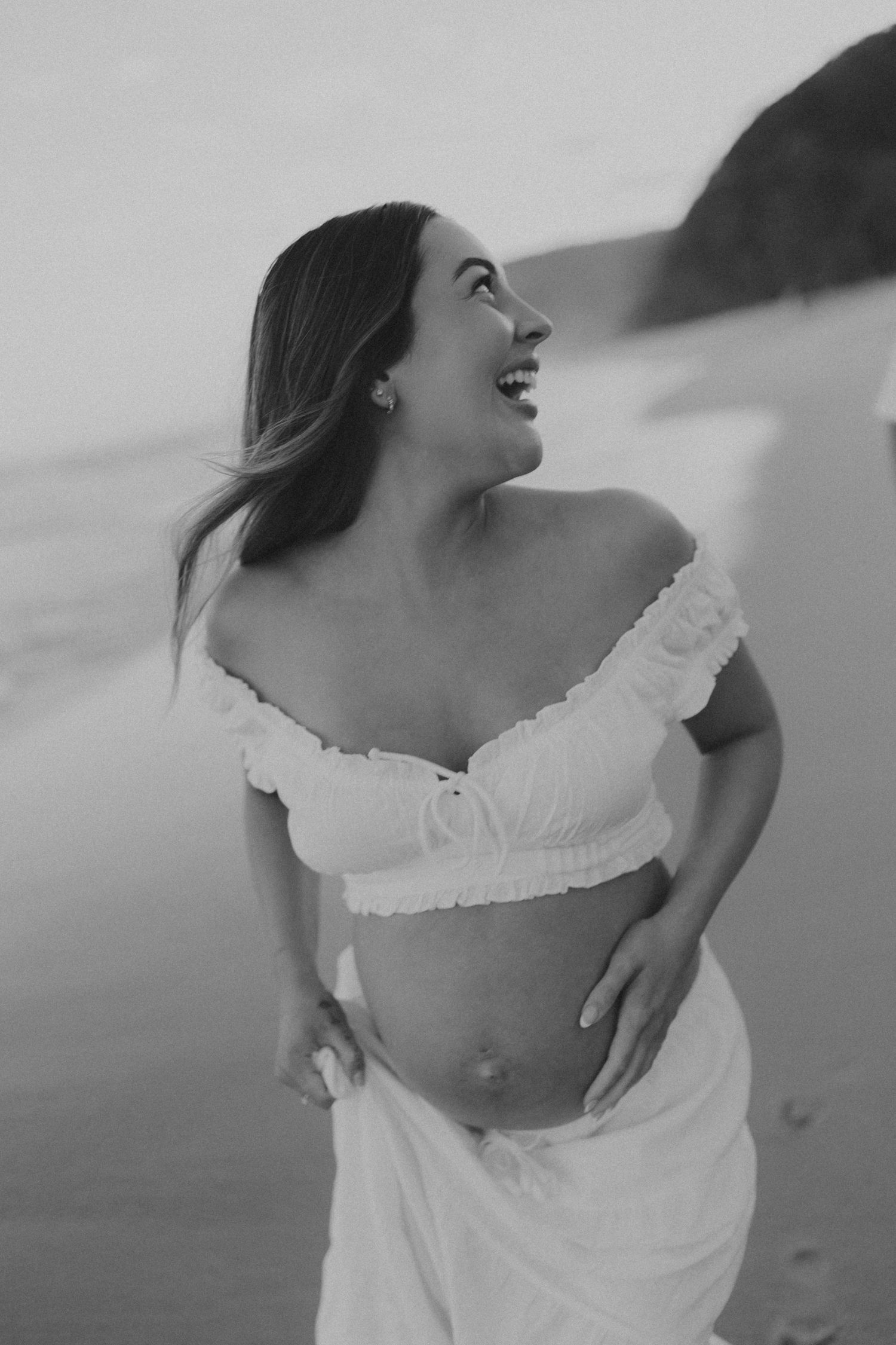 A series of black and white artistic portraits showing graceful movement and flowing white fabric on a beach.