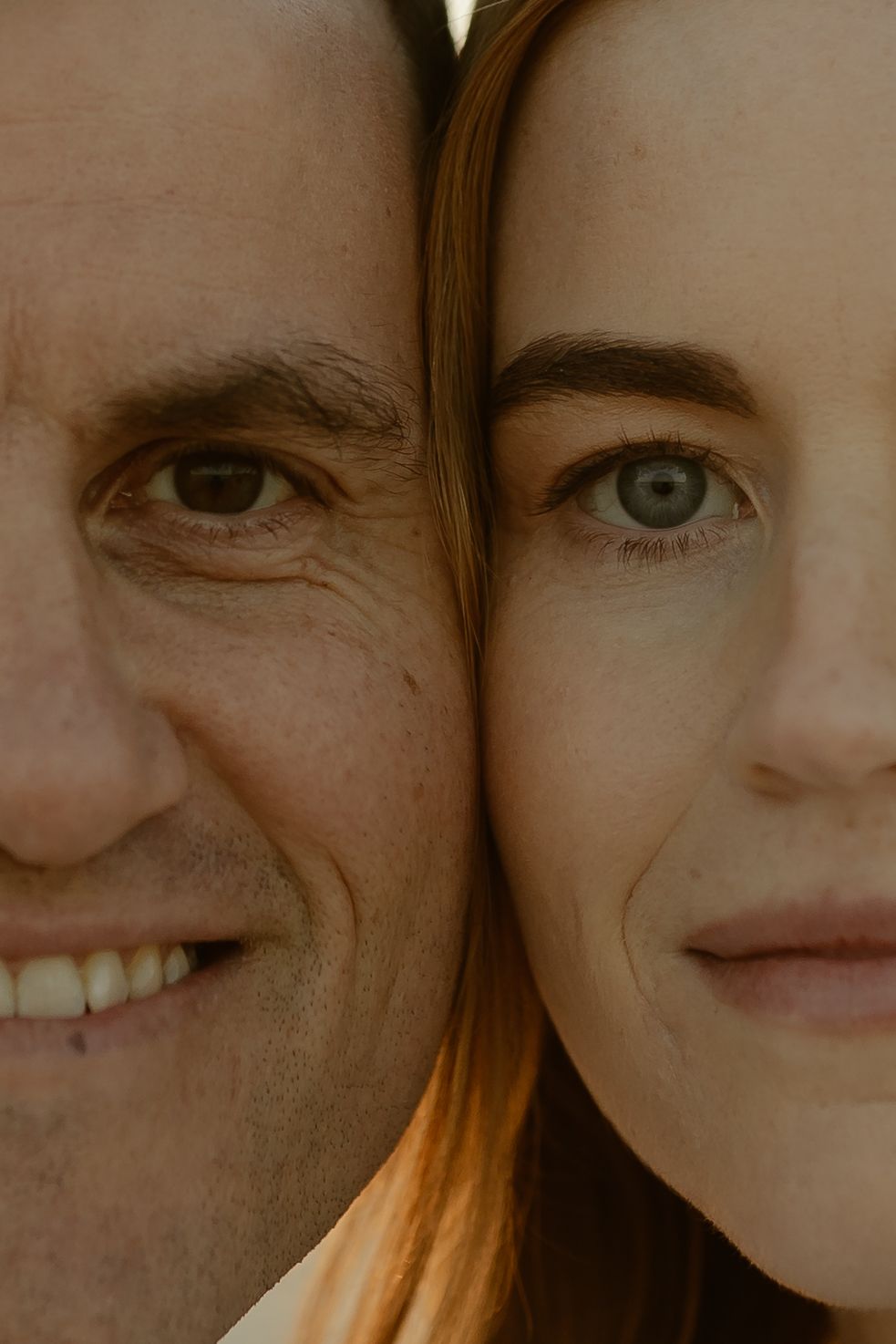 Close-up portrait of a smiling man and young woman with green eyes, cheeks touching, warm toned photo.