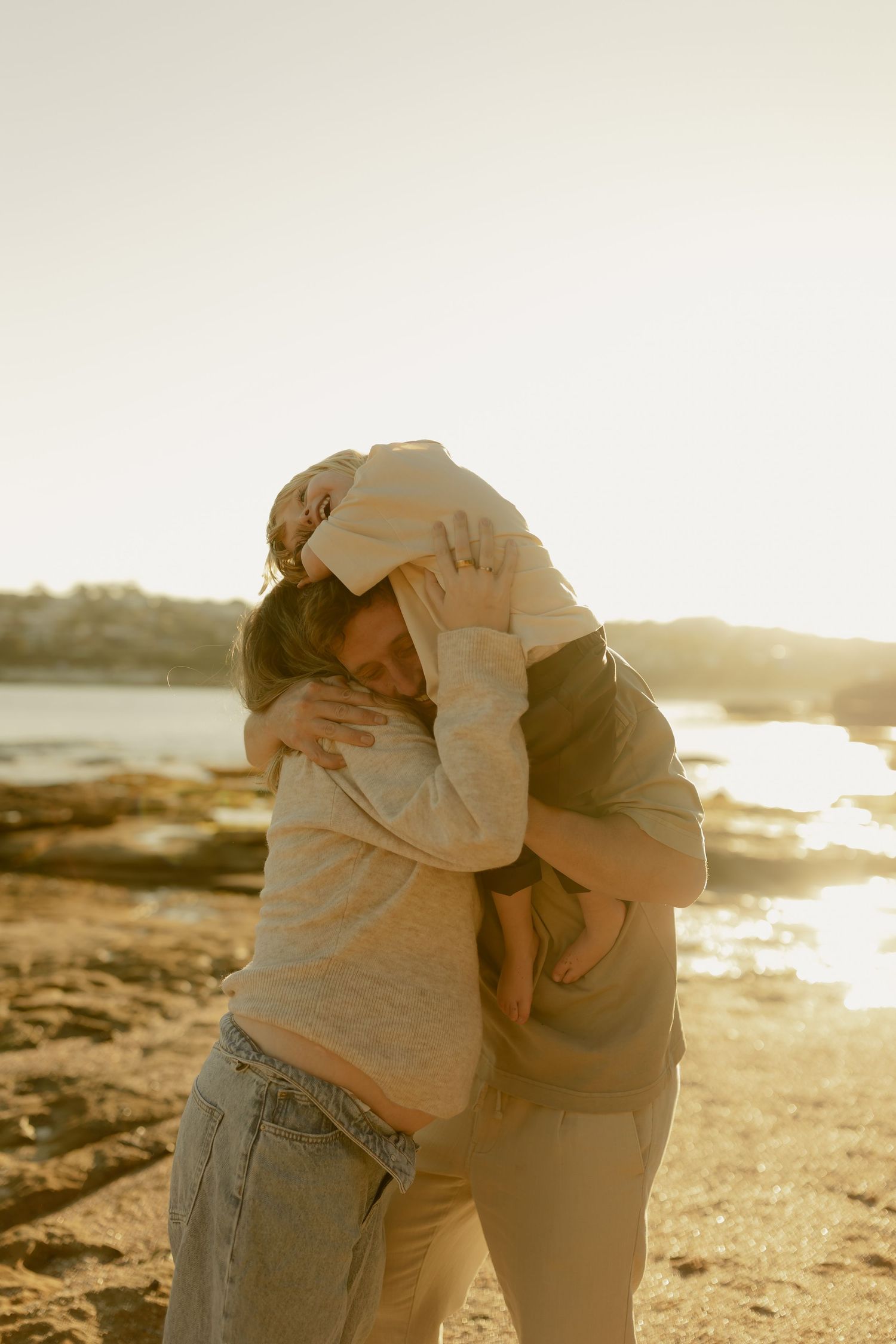 Two people sharing a tender embrace on rocky beach during glowing golden sunset.