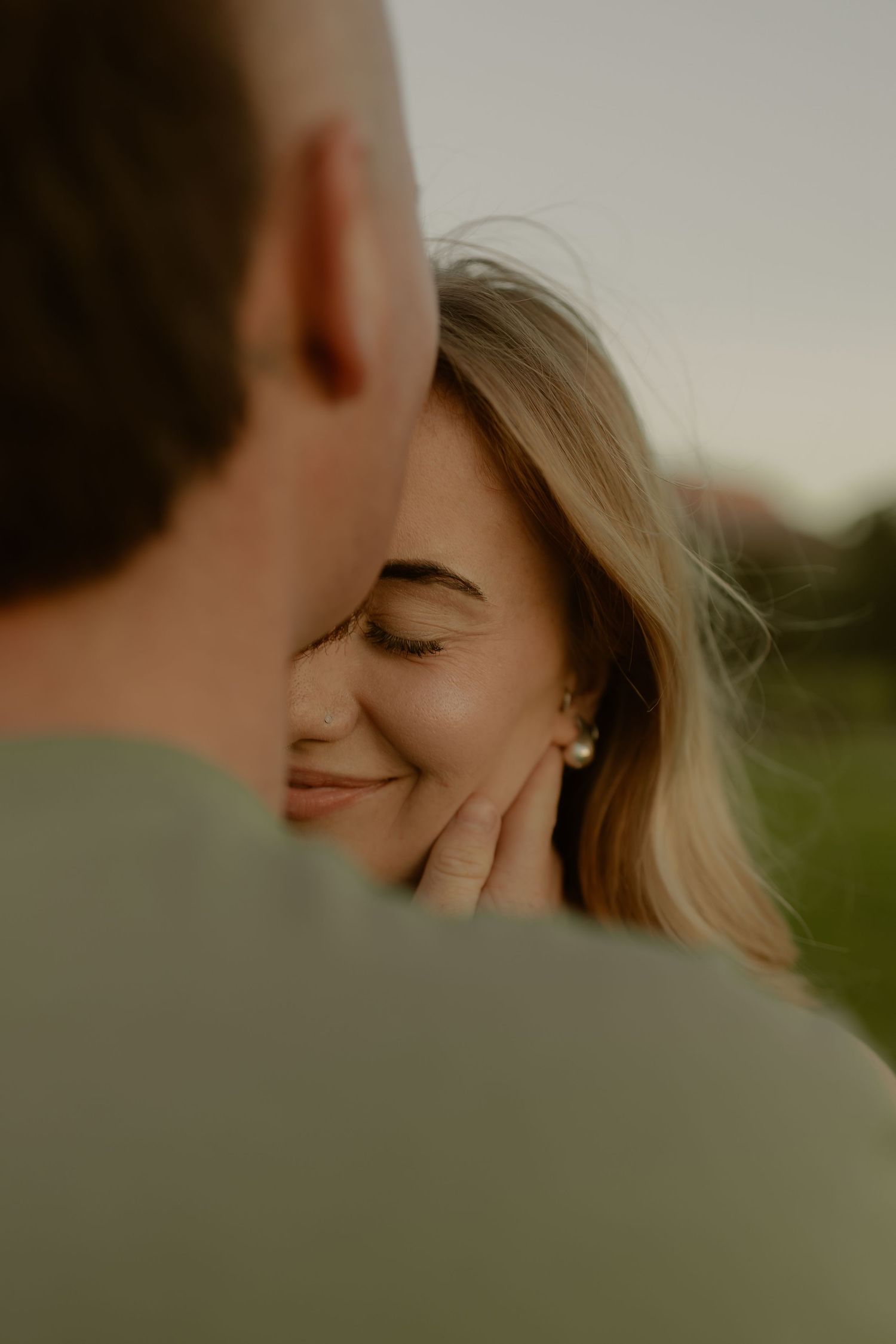 Close-up black and white photo of woman smiling with eyes closed as partner touches her face.
