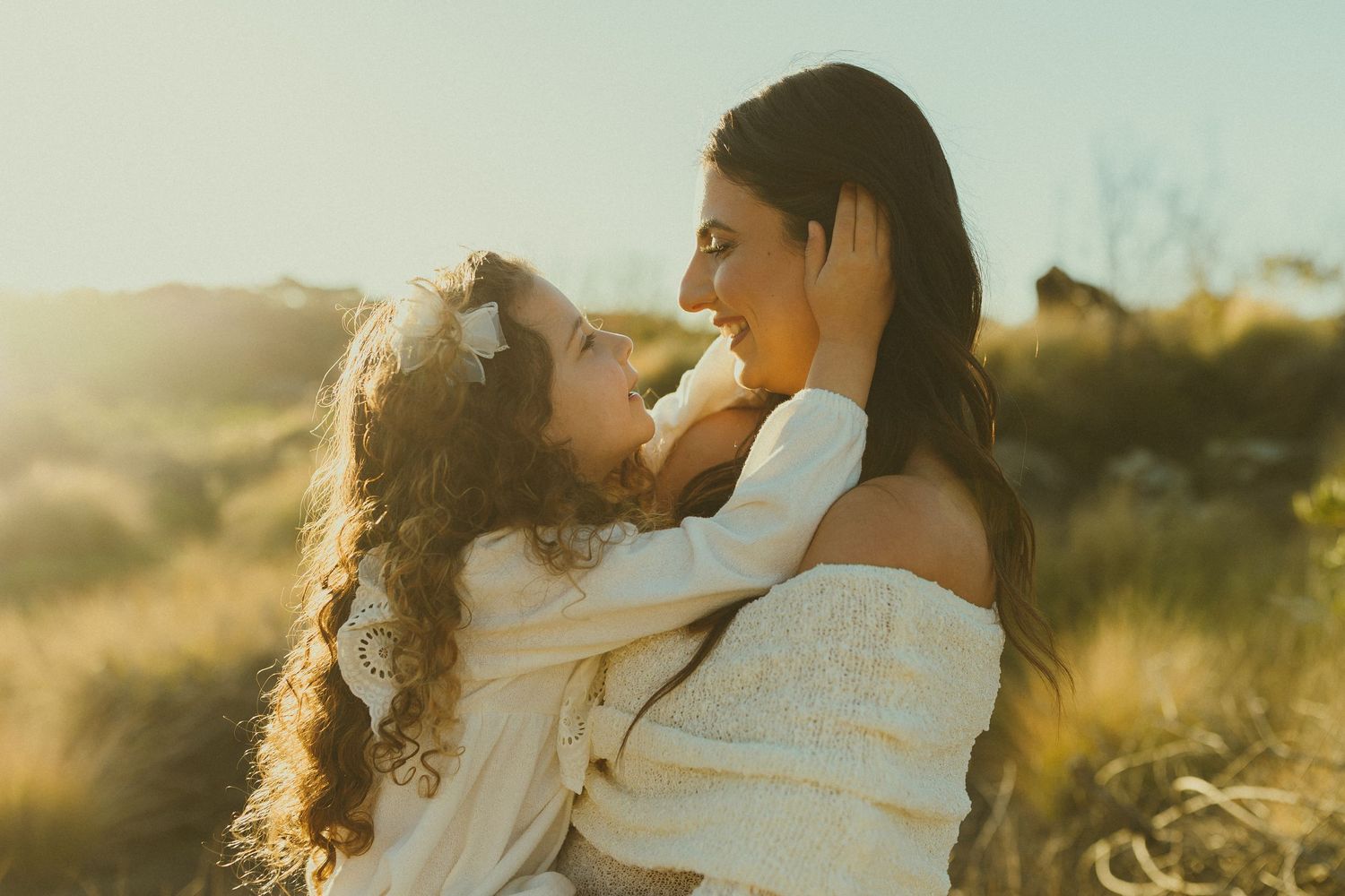 Mother and child sharing a tender moment in golden sunlight against a soft blurred natural backdrop.