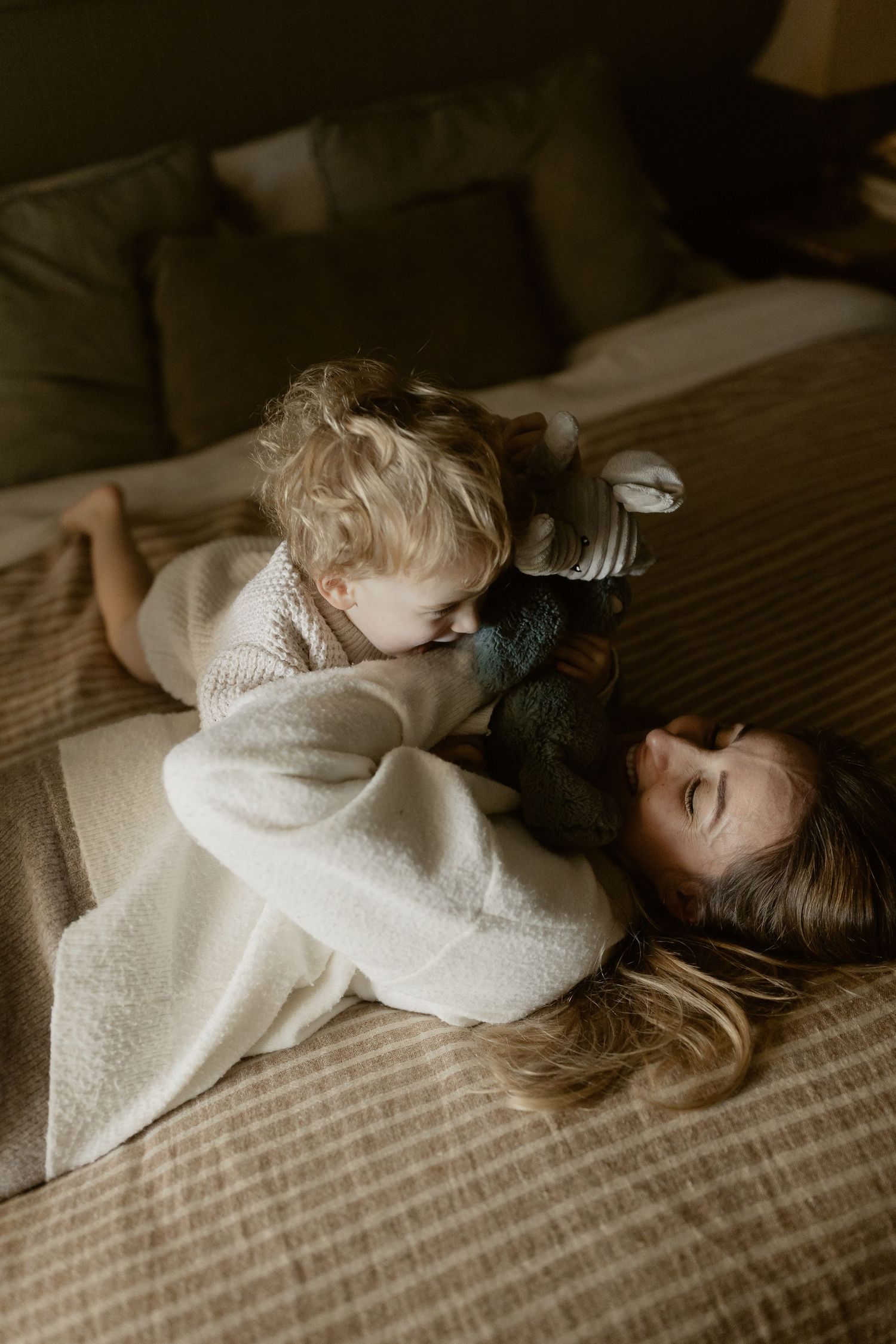 Intimate family moment showing cuddles and laughter on a cozy bed with white knit sweaters.