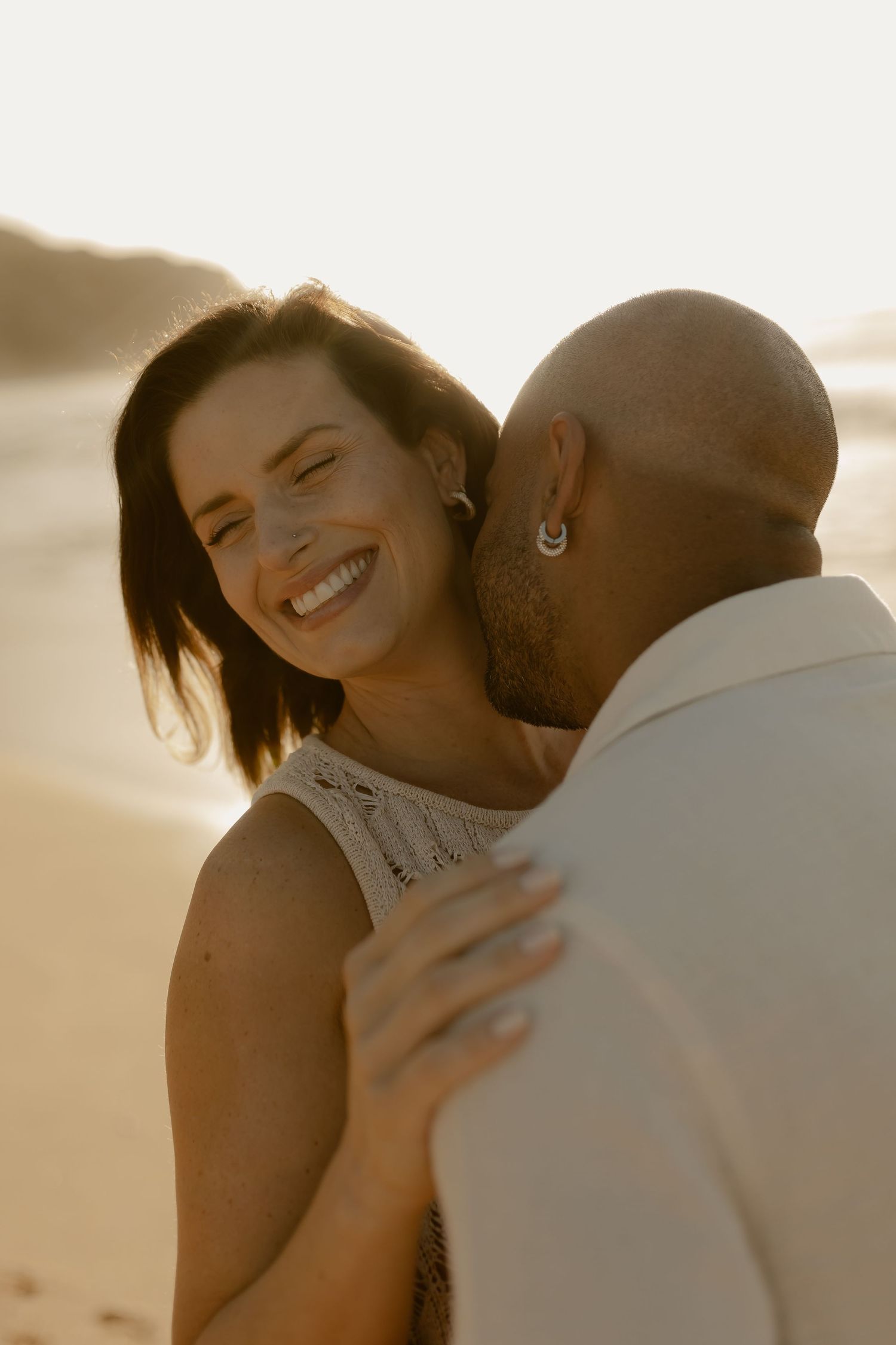 A couple embraces intimately on the beach during golden hour, creating a romantic silhouette against the sunset.