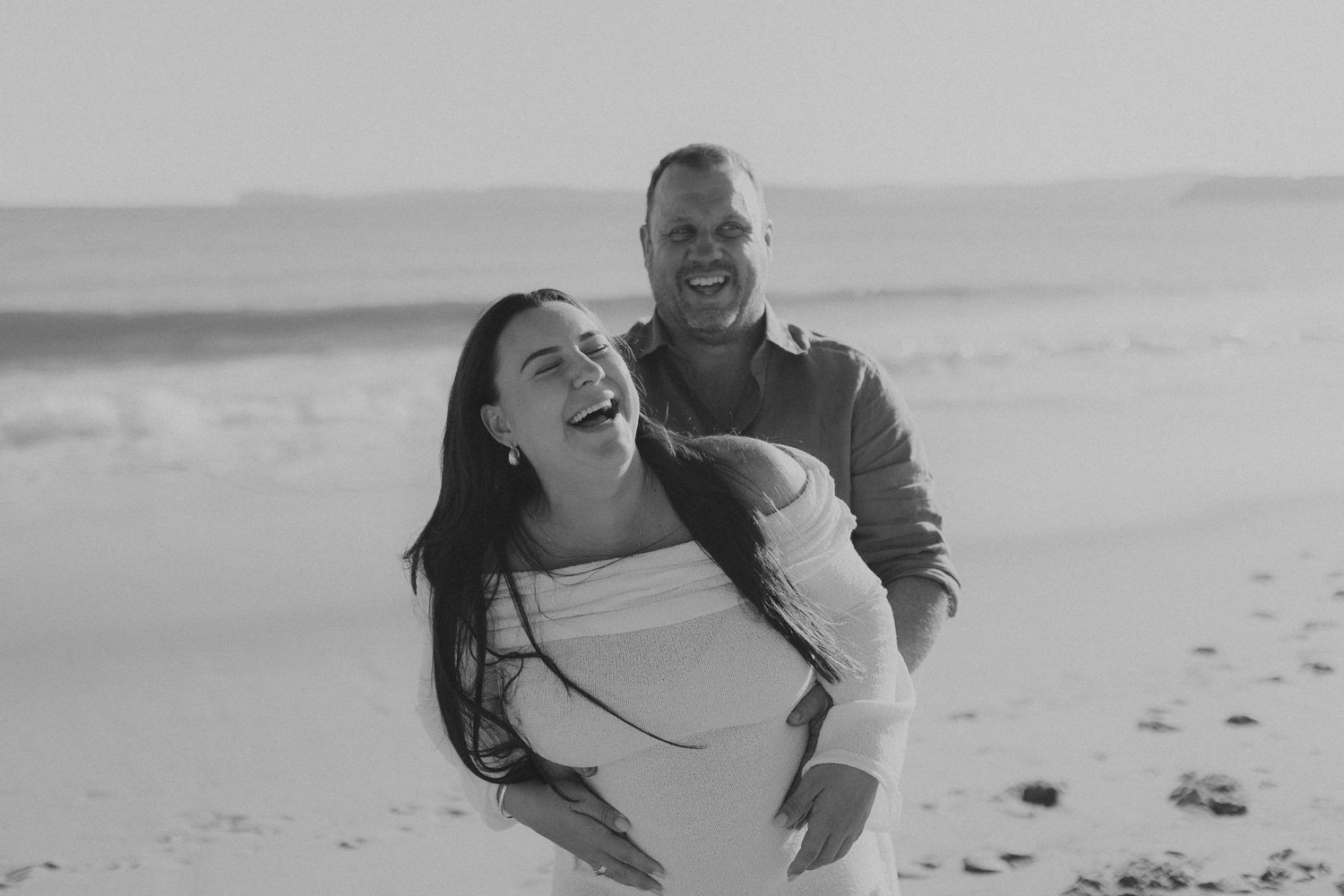 A romantic couple shares a playful moment together on a sandy beach.