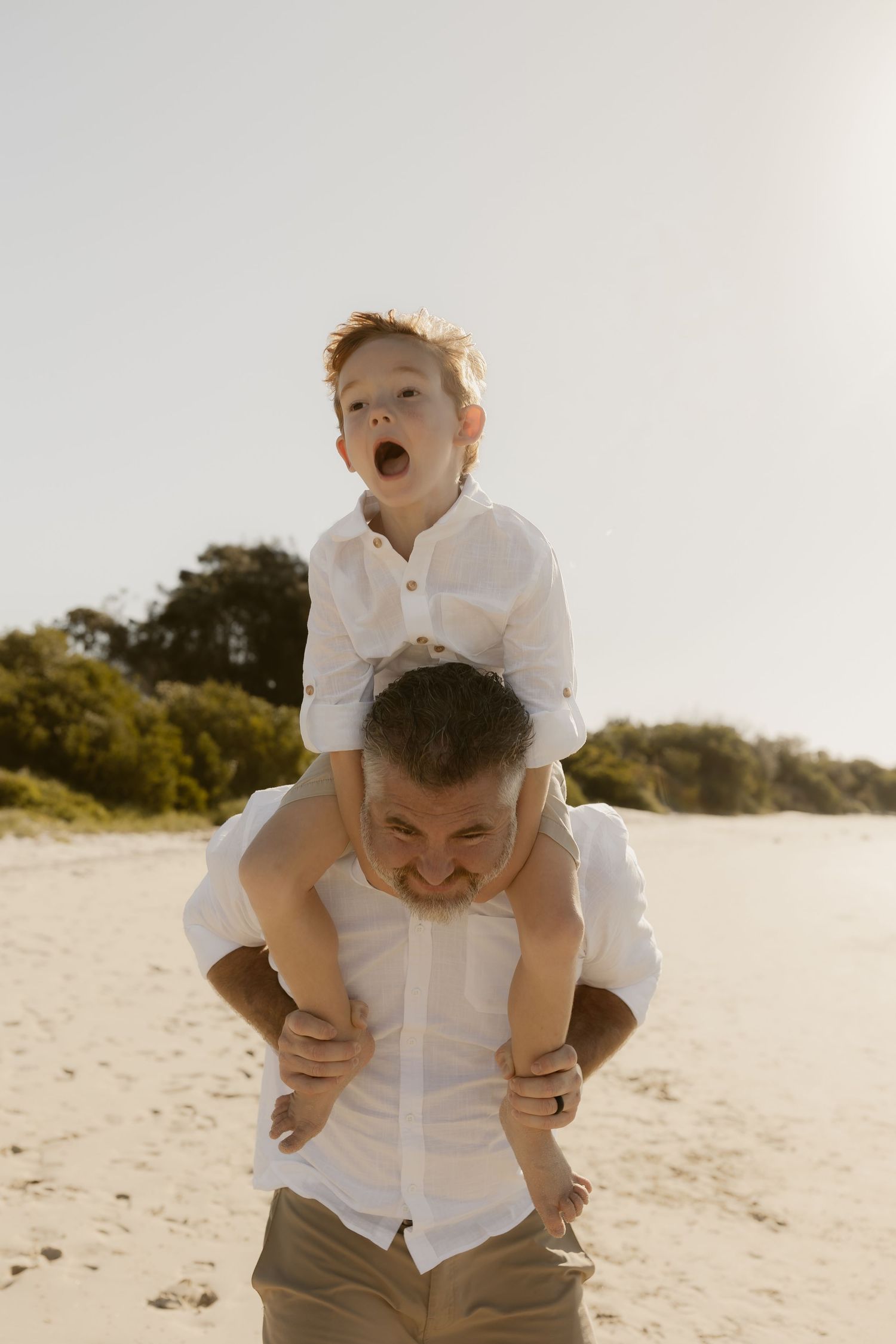 Playful piggyback ride moment on a sunny beach with casual attire and natural expressions.