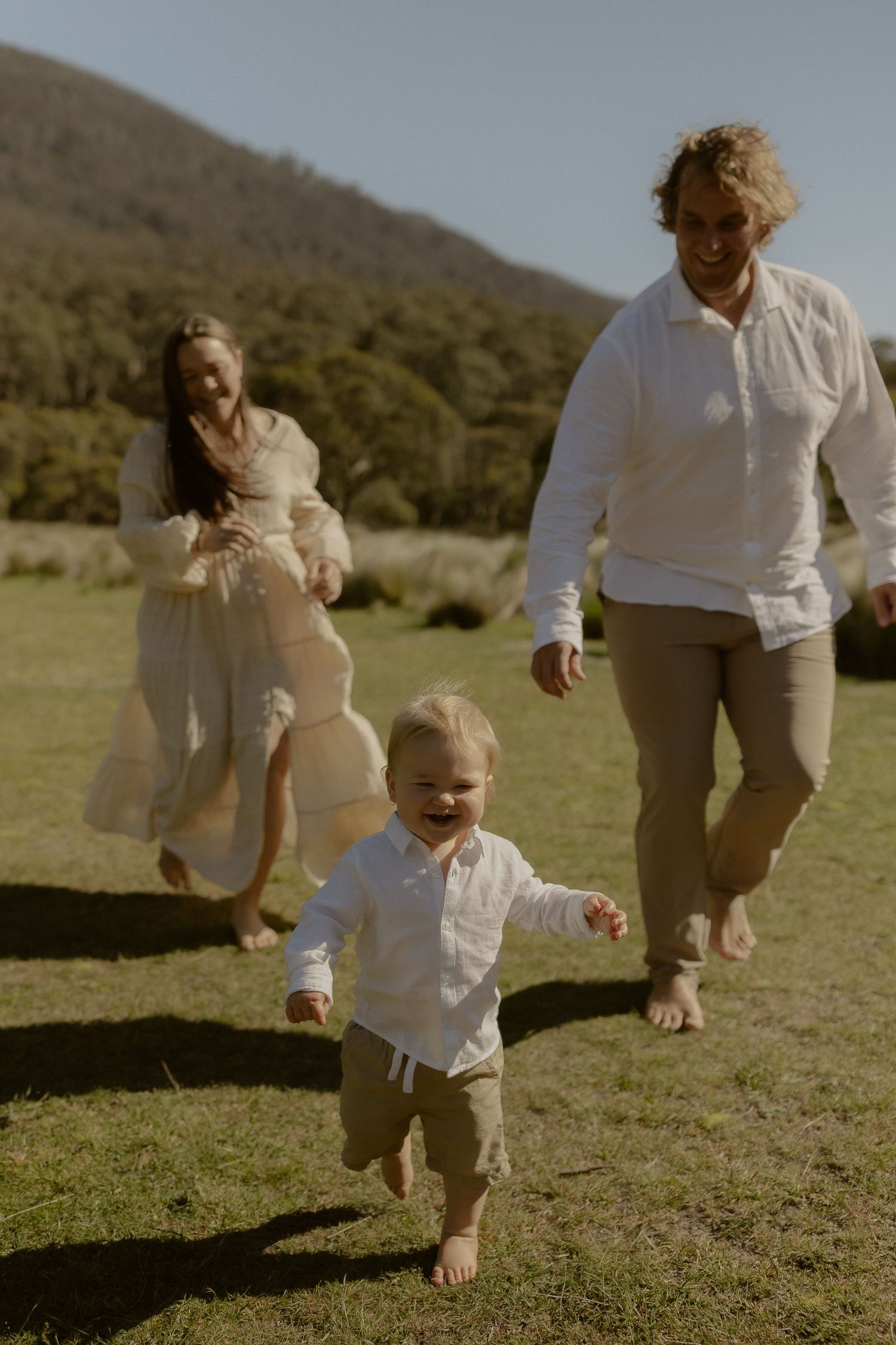 Family playing and running together on green grass with mountains in the distance.