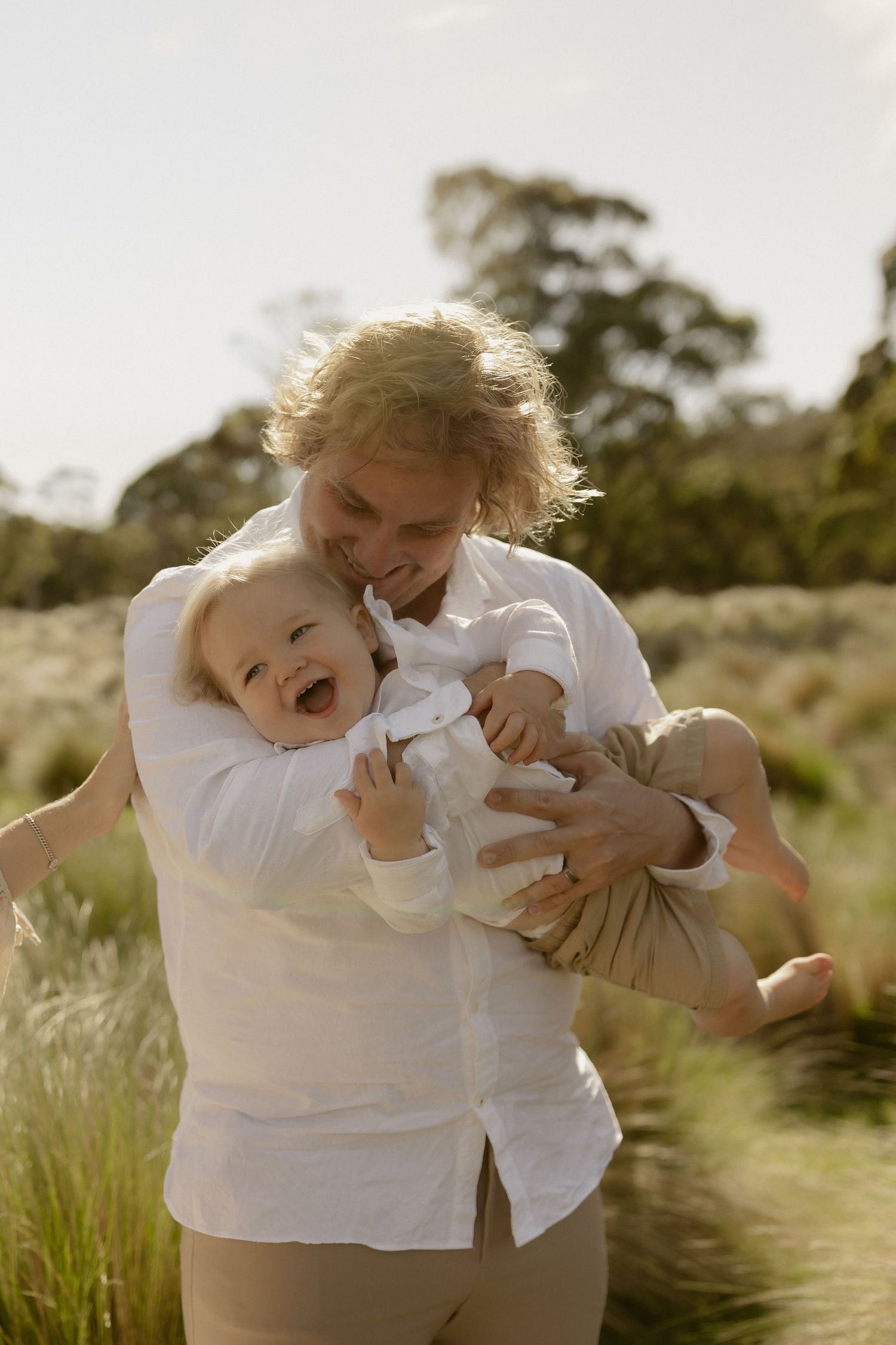 Candid sequence of playful moments between parent and child in white shirts laughing together in a sunlit meadow.