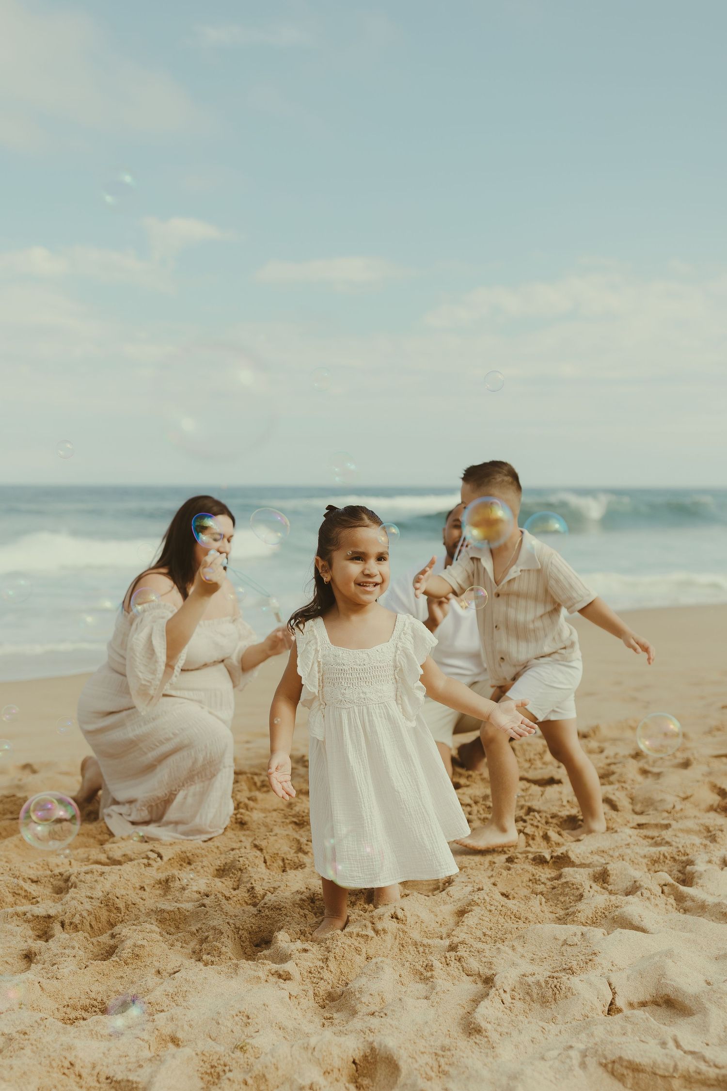A family in white outfits plays together on a sunny beach, creating joyful moments in the sand.