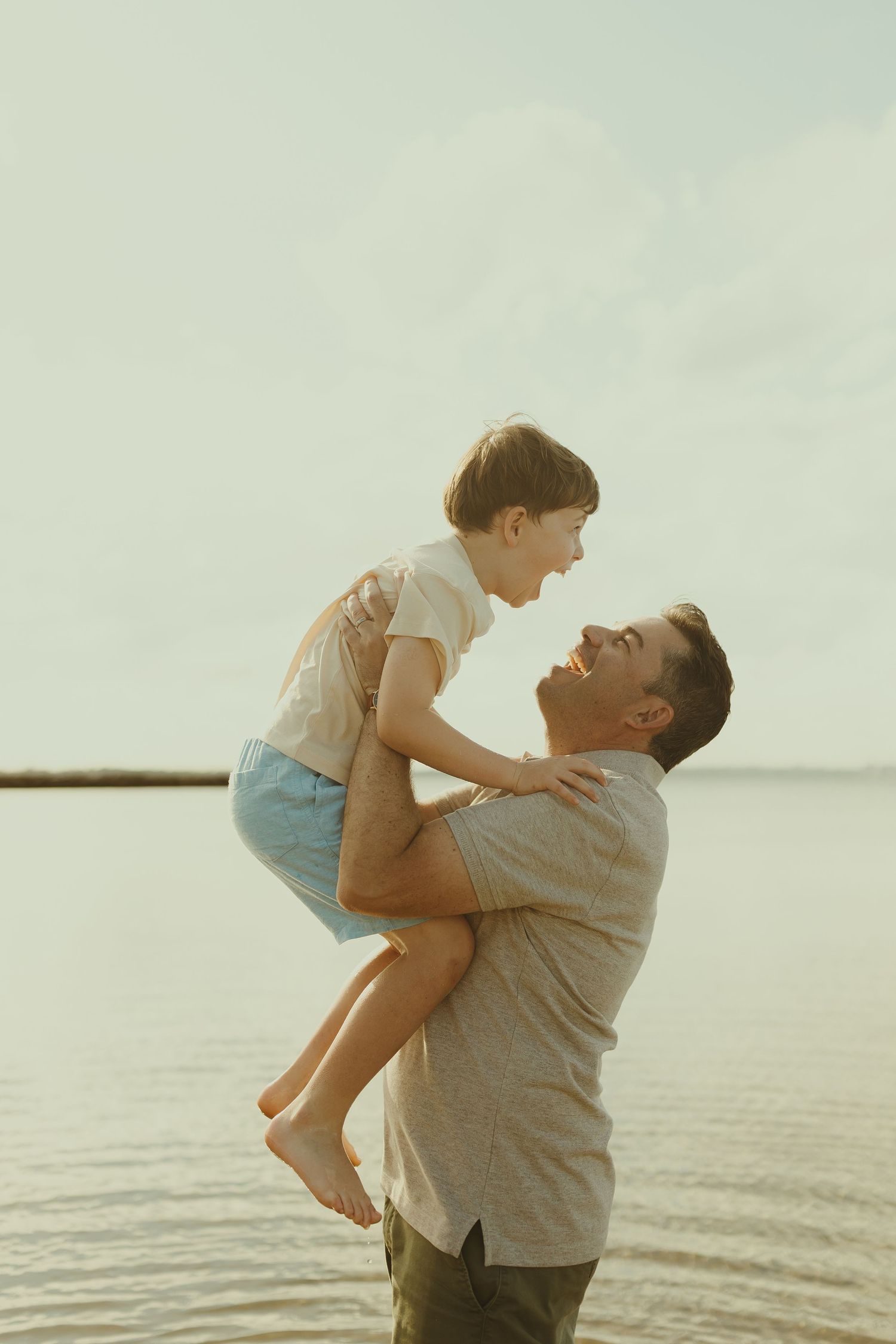 A parent and child share a joyful moment playing together at the beach during sunset.