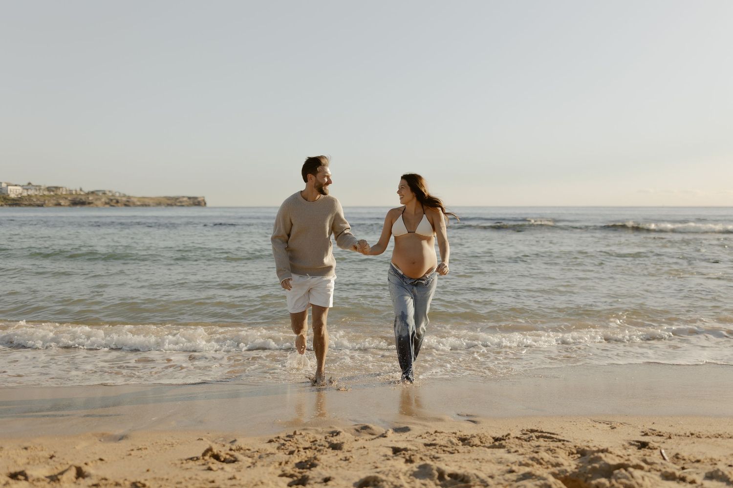 Couple walking hand in hand along the ocean shore at dusk.