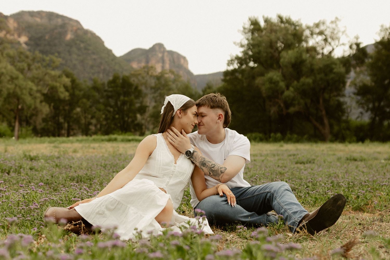 A couple shares intimate moments while laying in a grassy field during a romantic outdoor photo session.