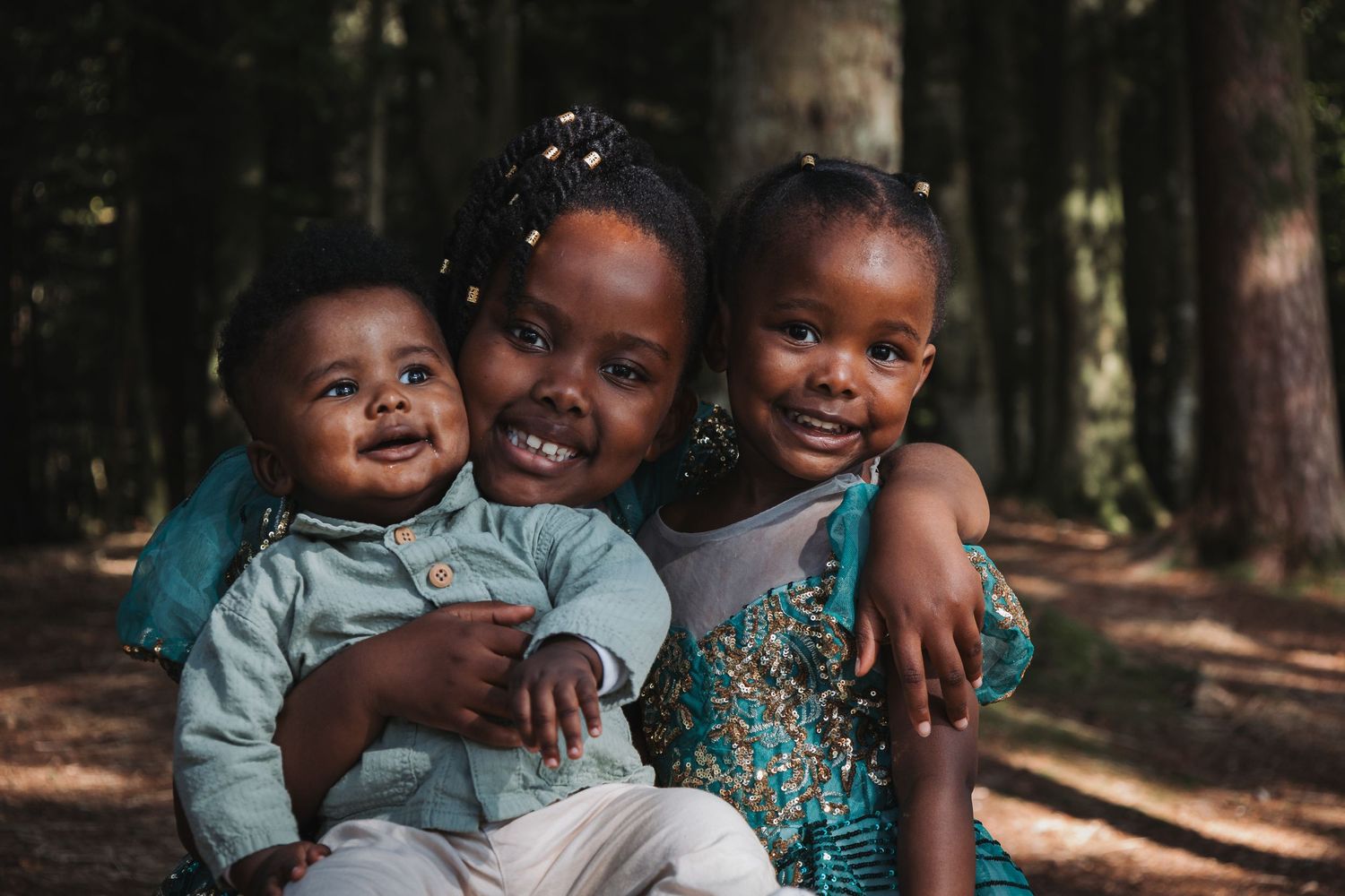 Three children in casual attire share joyful moment together in forest setting.