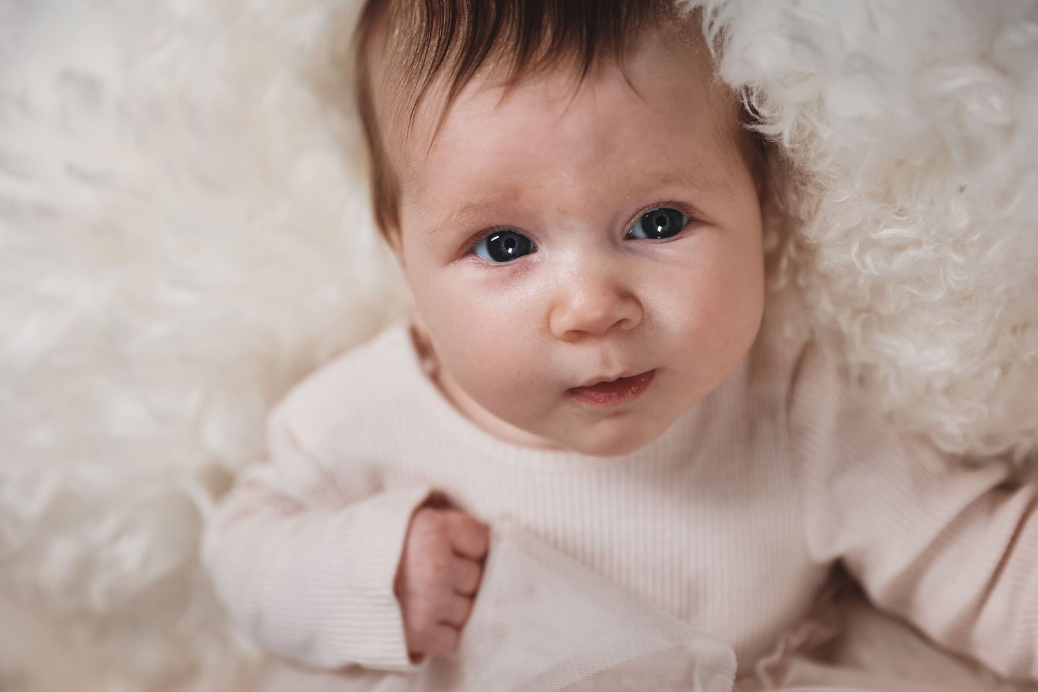 Baby in cream sweater smiling against soft white textured background.