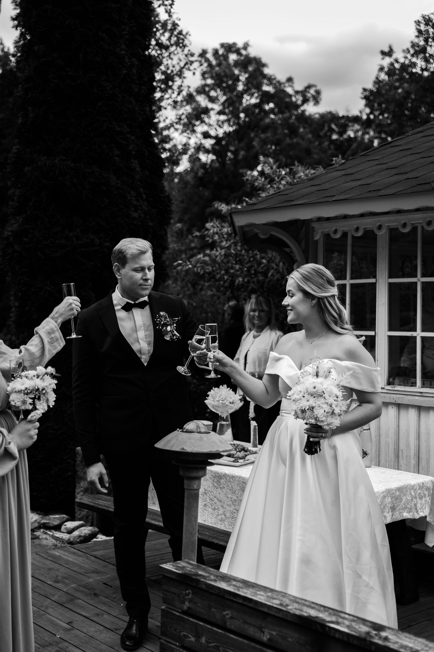 Black and white photo of a bride and groom toasting with champagne glasses at an outdoor wedding reception.