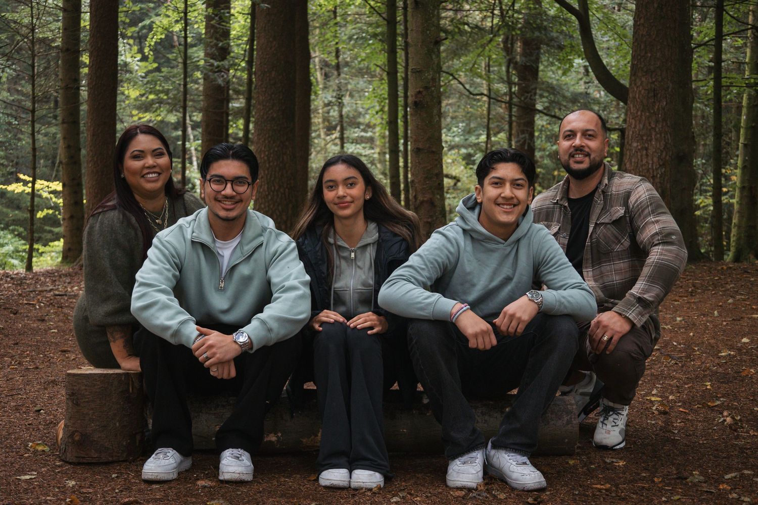 A group sits together on a wooden log in a dense evergreen forest.