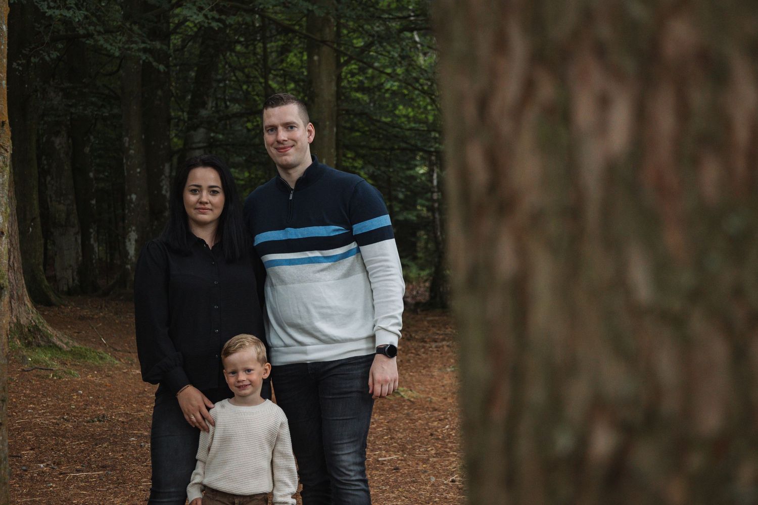 A casual family portrait taken on a forest trail surrounded by towering trees.