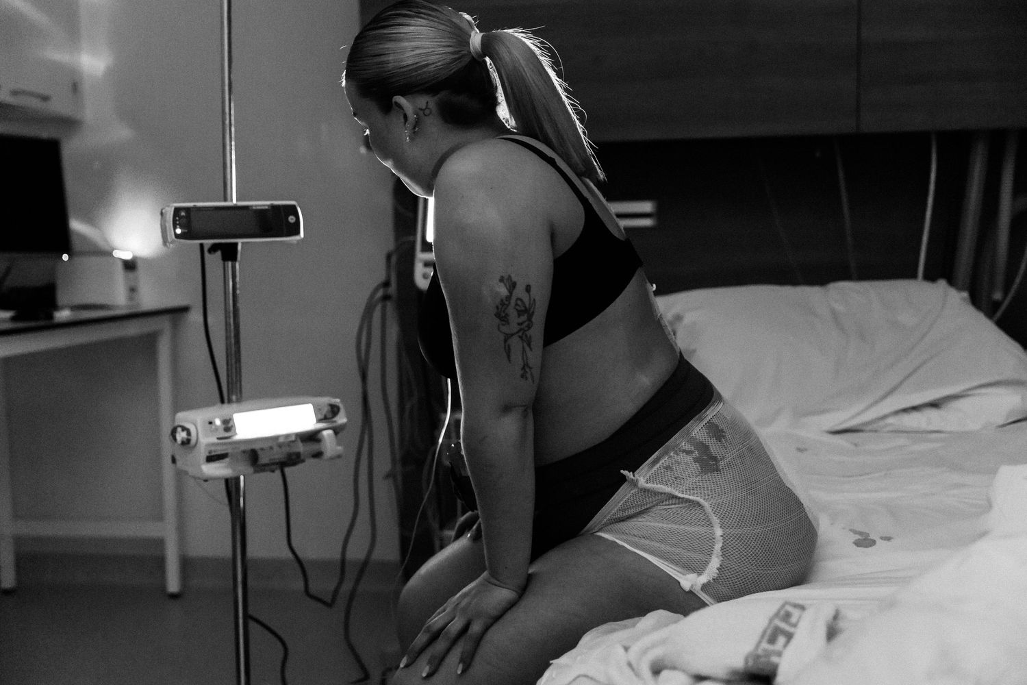 Black and white image showing a patient sitting on a hospital bed next to medical monitoring equipment.