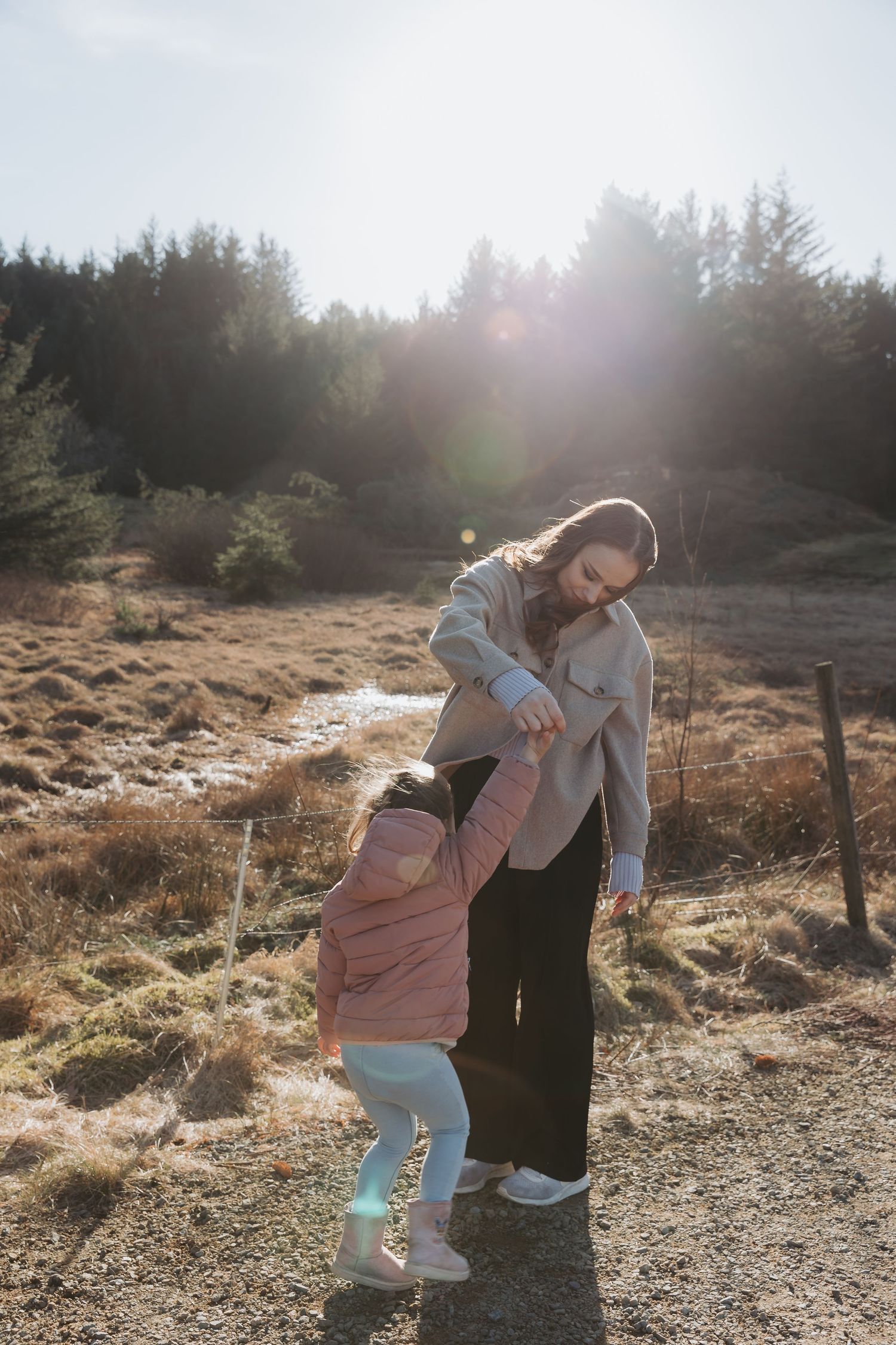 A caretaker and child playing together on a sunlit forest trail during a hike on a misty afternoon.