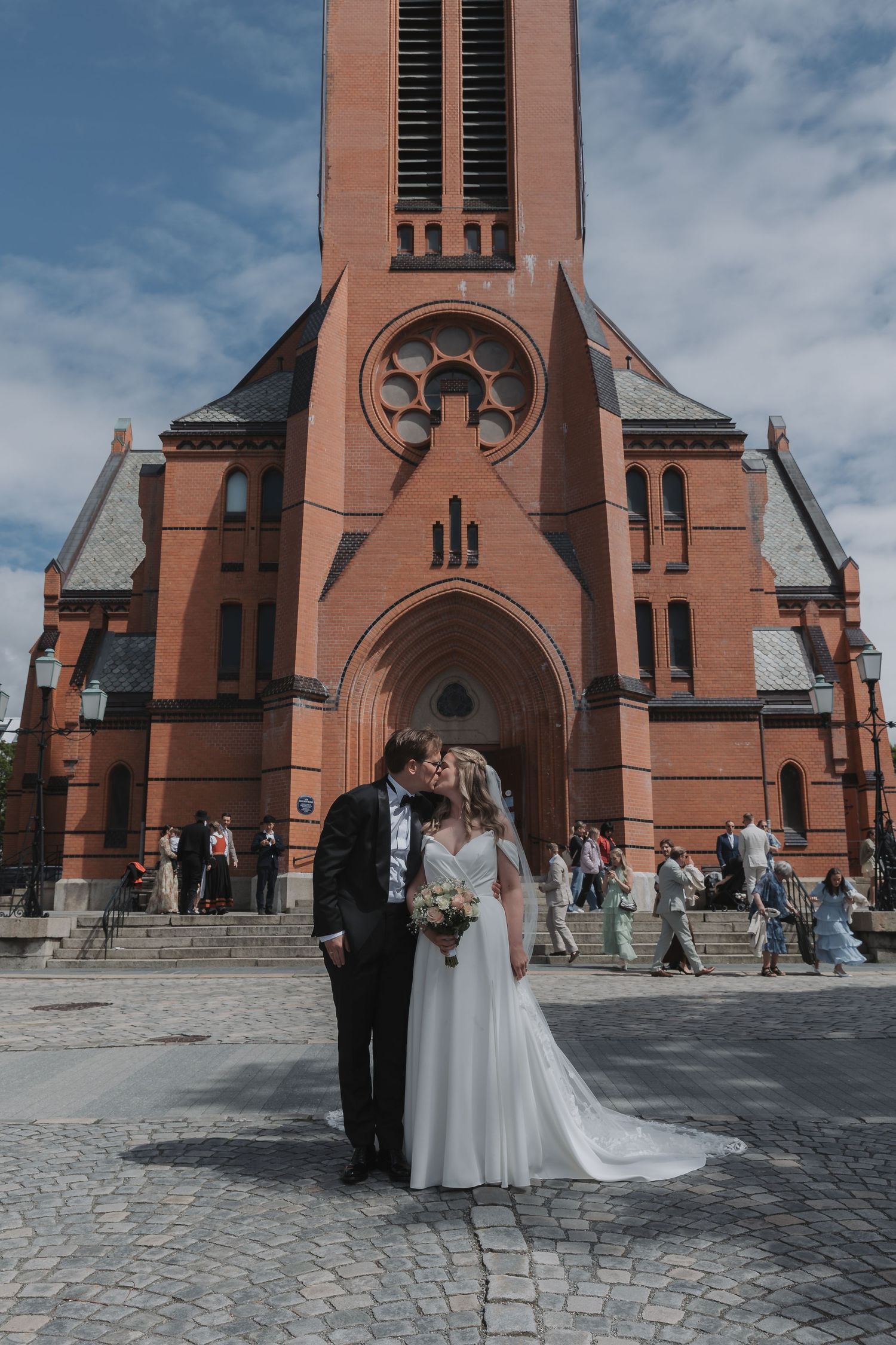 Bride and groom kissing in front of a grand red brick church on their wedding day.