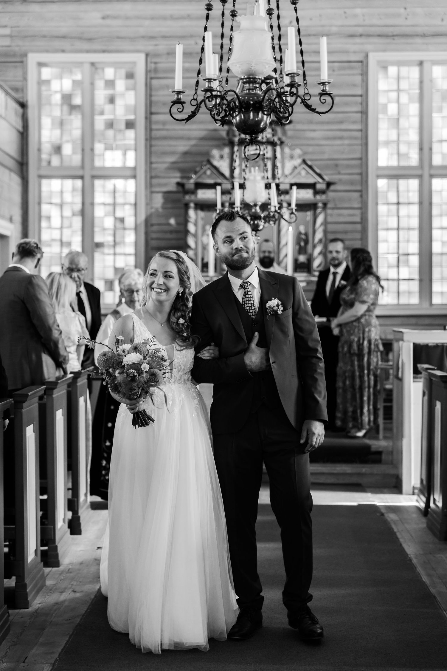 Black and white photo of a smiling bride and groom walking down the church aisle after their wedding ceremony.