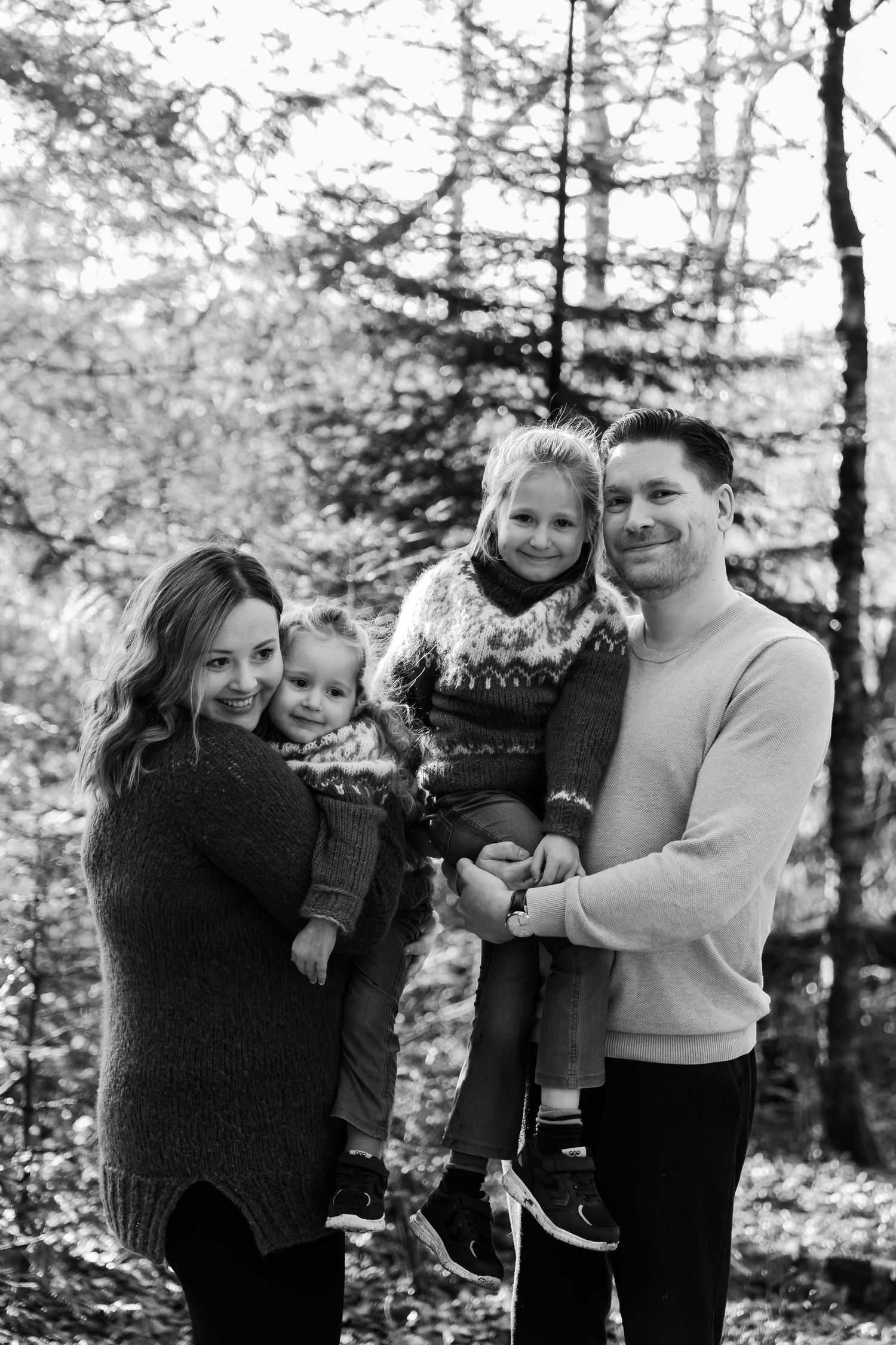 Black and white family portrait series showing loving embraces and joyful moments in a wooded outdoor setting.