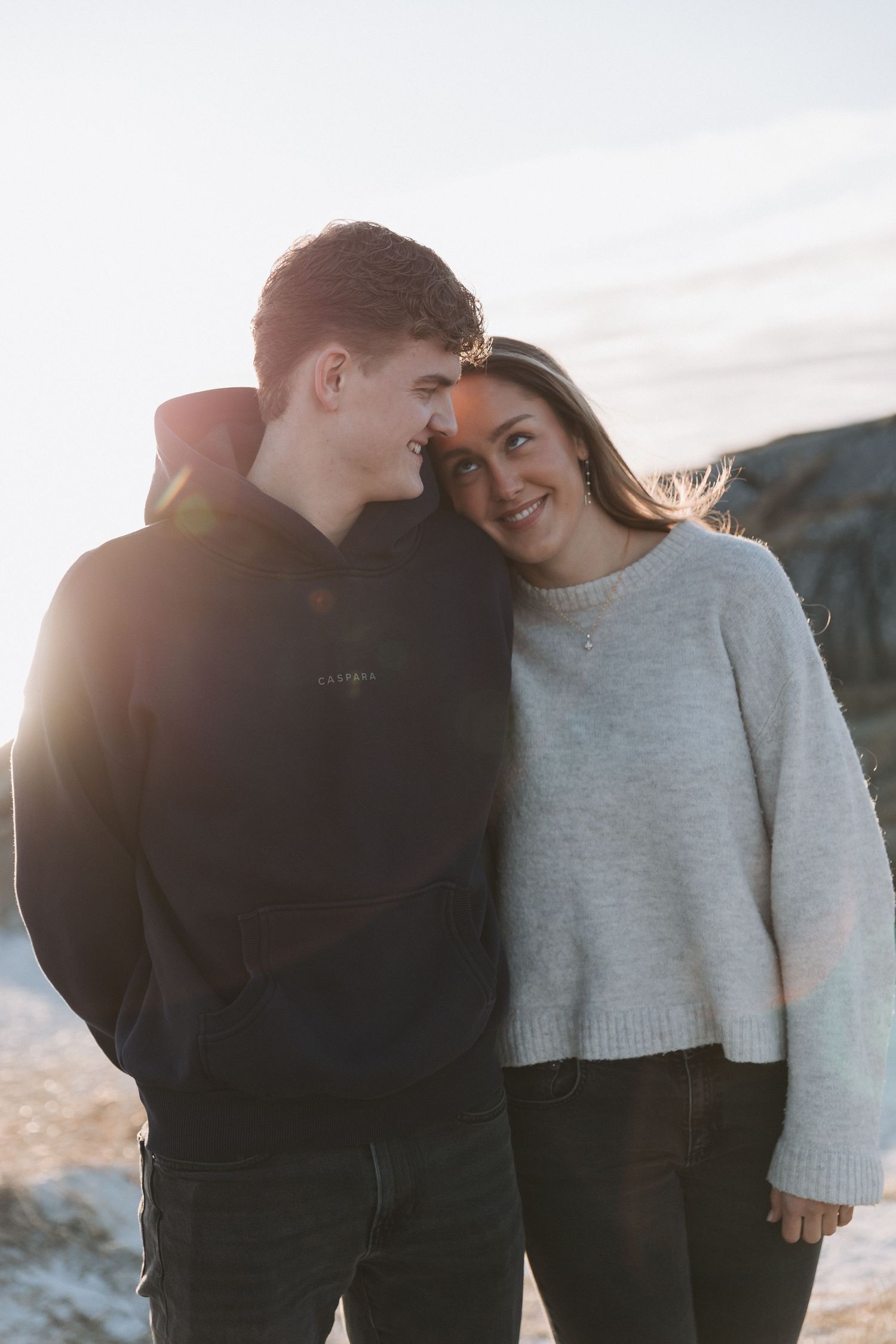 Young couple sharing a romantic moment outdoors at sunset, smiling at each other in casual winter clothing.
