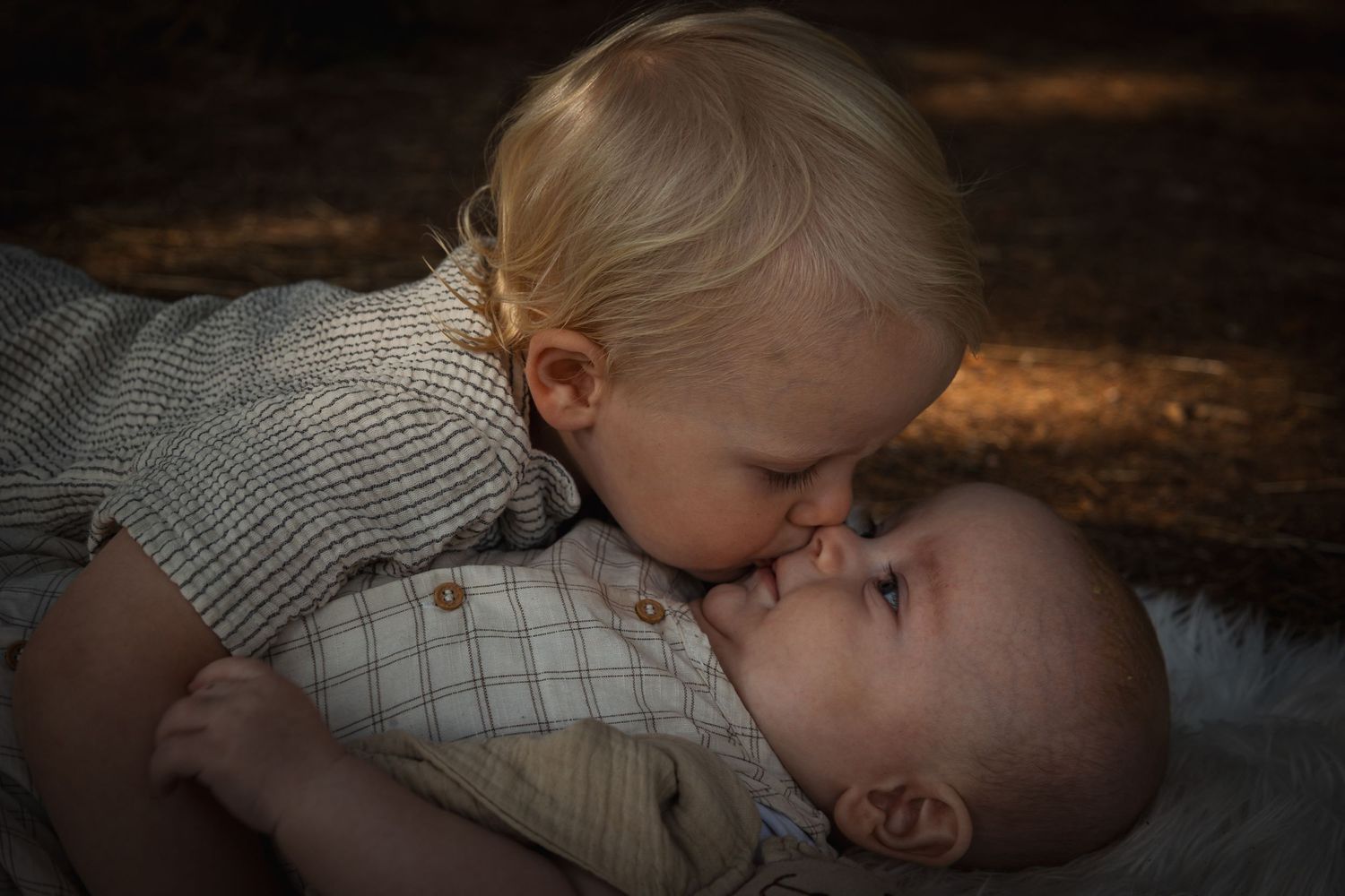 Sweet moment of tender affection between two siblings in a wooded setting with warm lighting.
