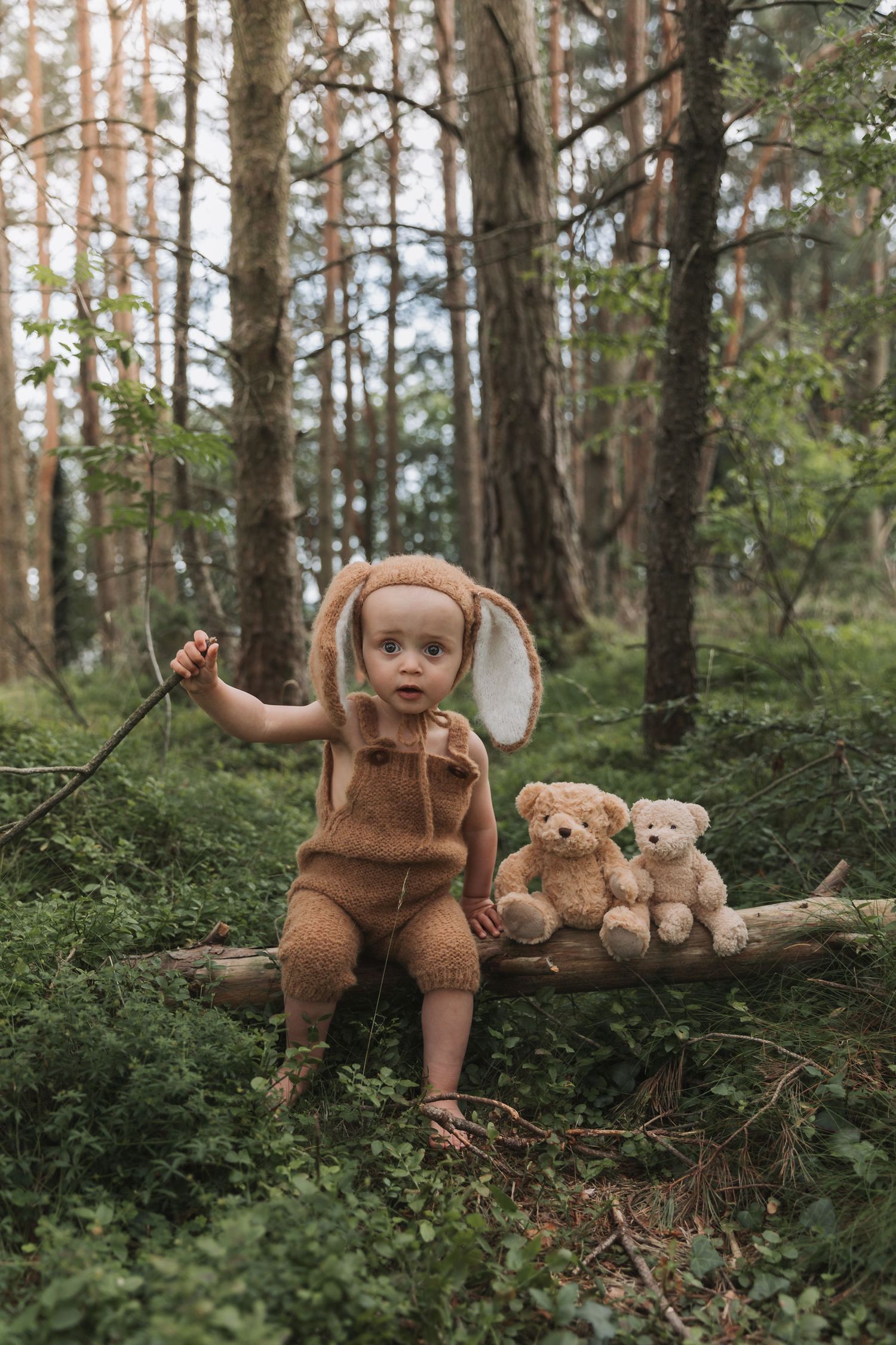 Three matching photos of a baby doll and teddy bears arranged on a fallen log in a moody forest setting.