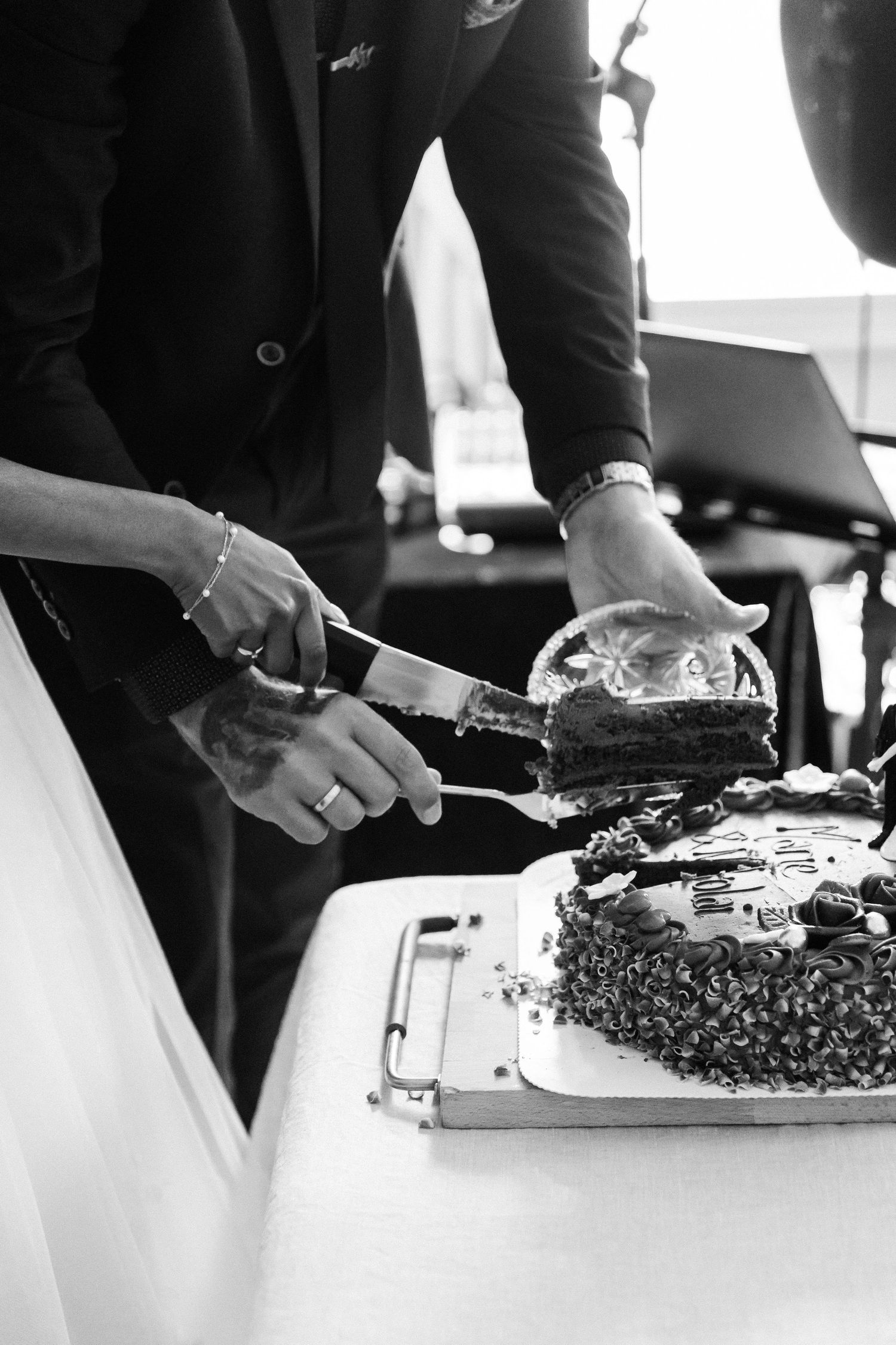 Black and white photo of bride and groom cutting a decorated wedding cake together at their reception.