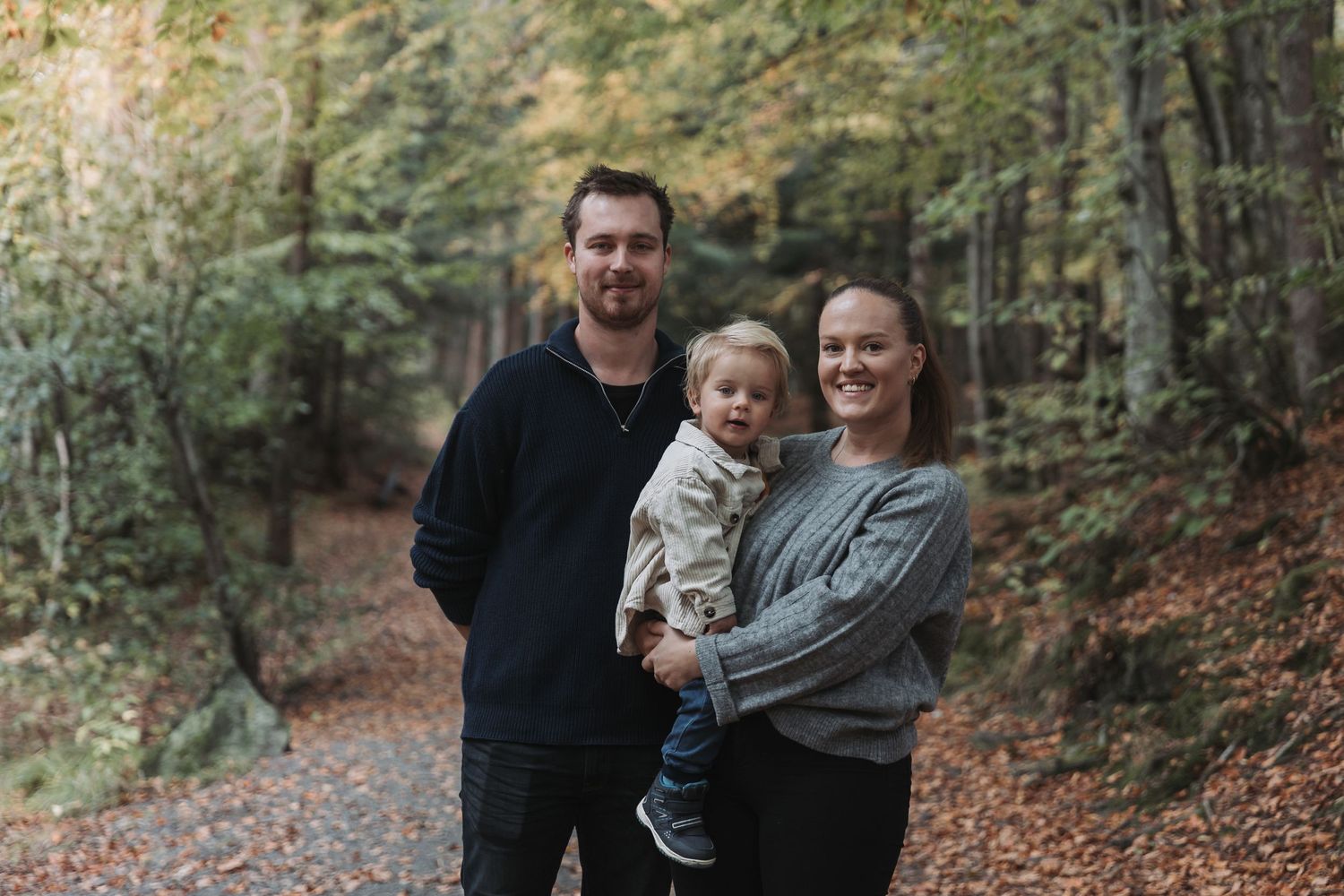 A relaxed family portrait taken on a wooded trail during autumn.