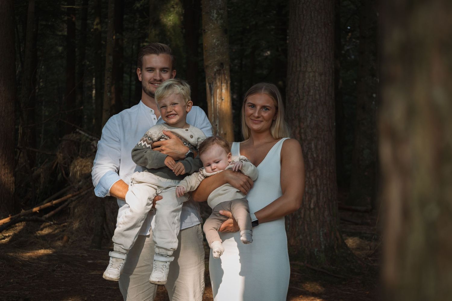 A family portrait captured in a serene forest setting with sunlight filtering through the trees.
