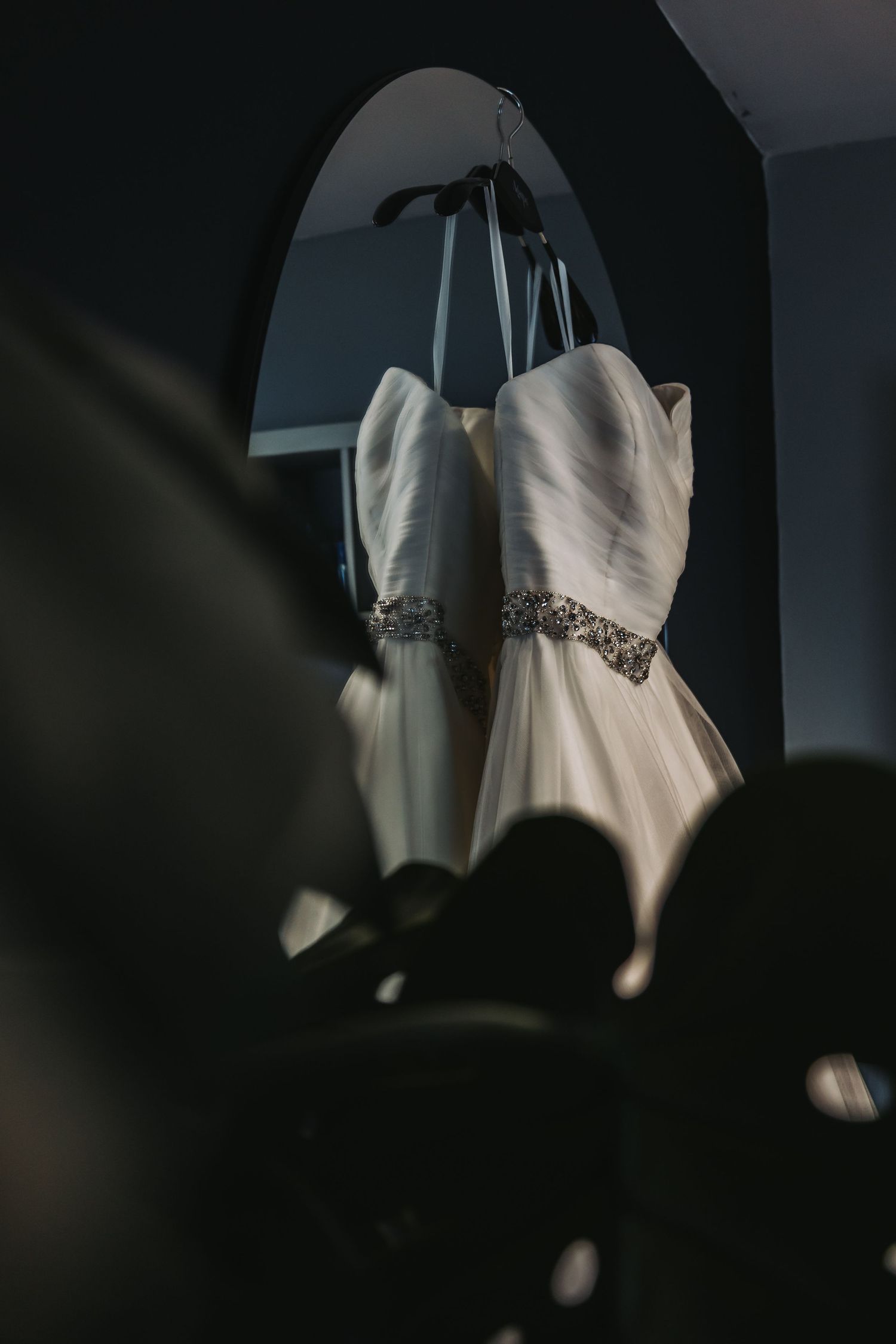 White wedding dresses with embellished waistbands hanging in dark room.
