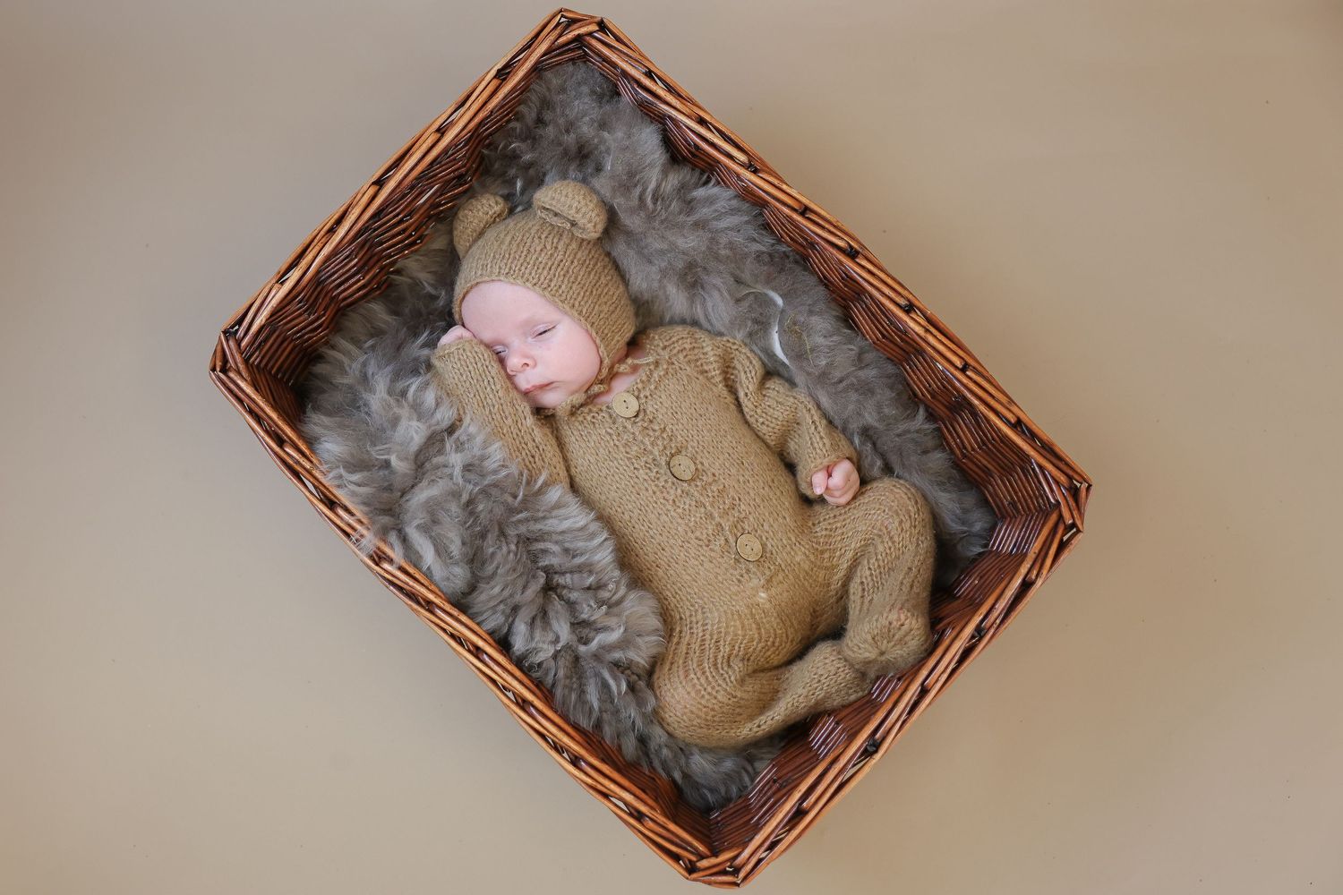 Gray kitten sleeps curled up in wicker basket on beige surface.