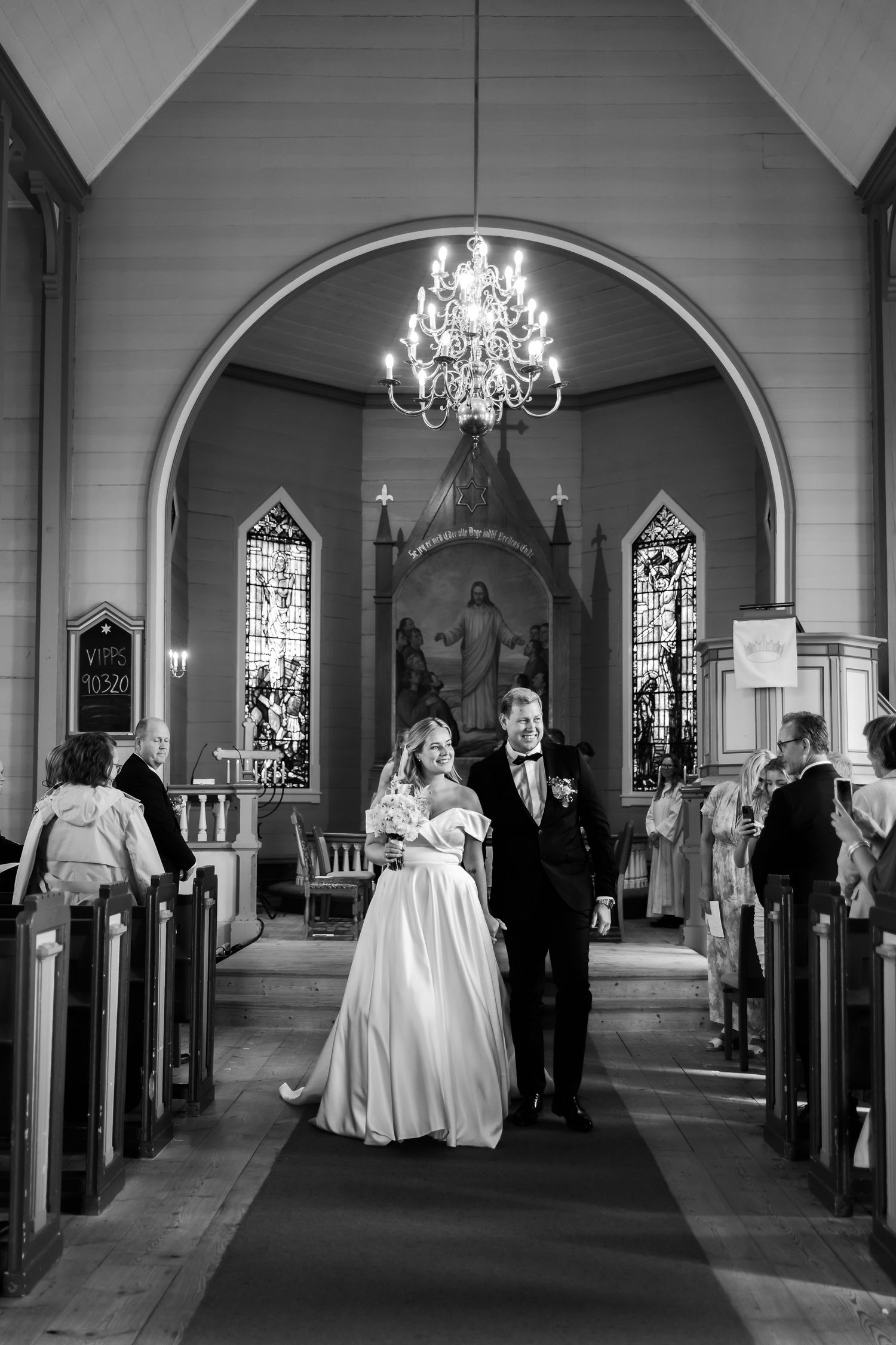 Black and white photo of a bride and groom walking down the aisle of a historic church after their wedding ceremony.