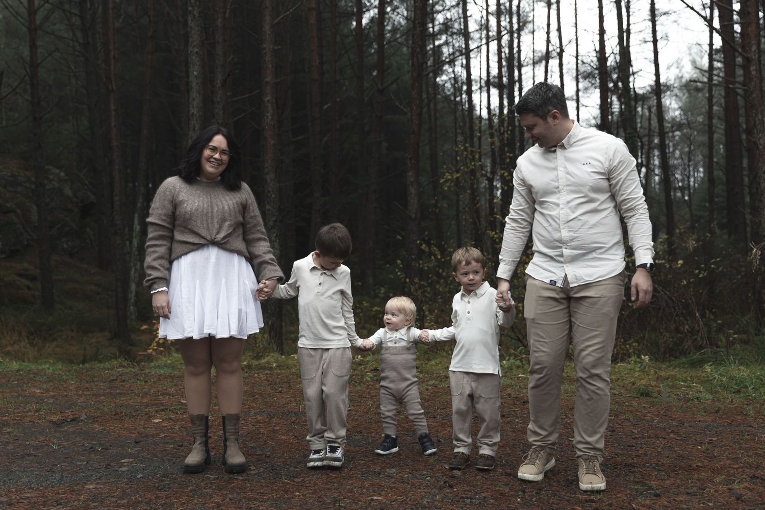 Family of five walking hand-in-hand on a forest path, dressed in coordinating neutral tones for a professional photo session.