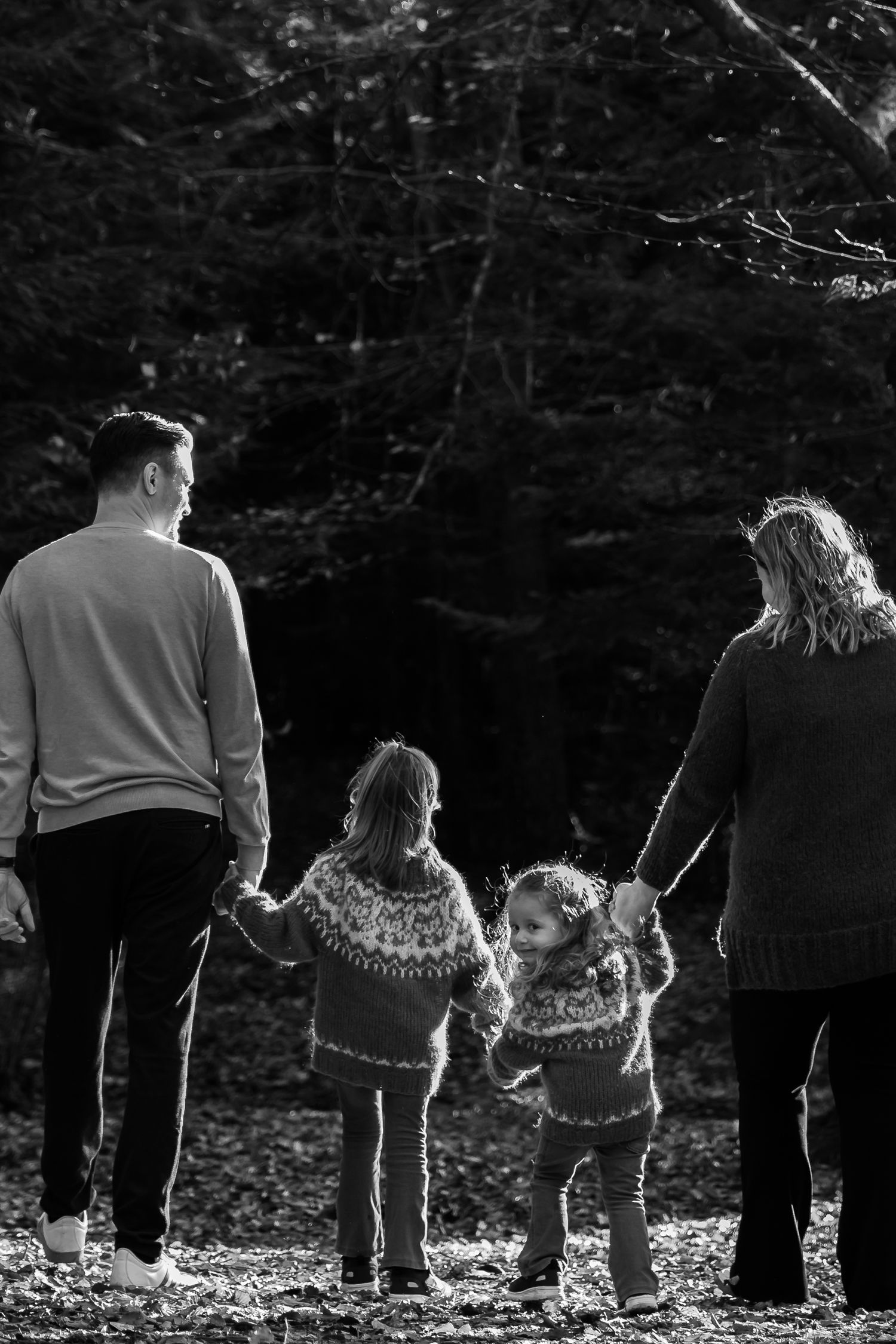 Black and white photo of a family holding hands while walking together in a forest wearing matching sweaters.