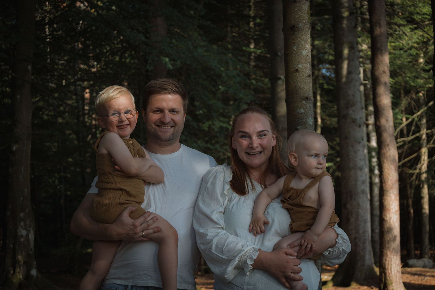 A family photo taken in a lush forest with tall evergreen trees in the background.