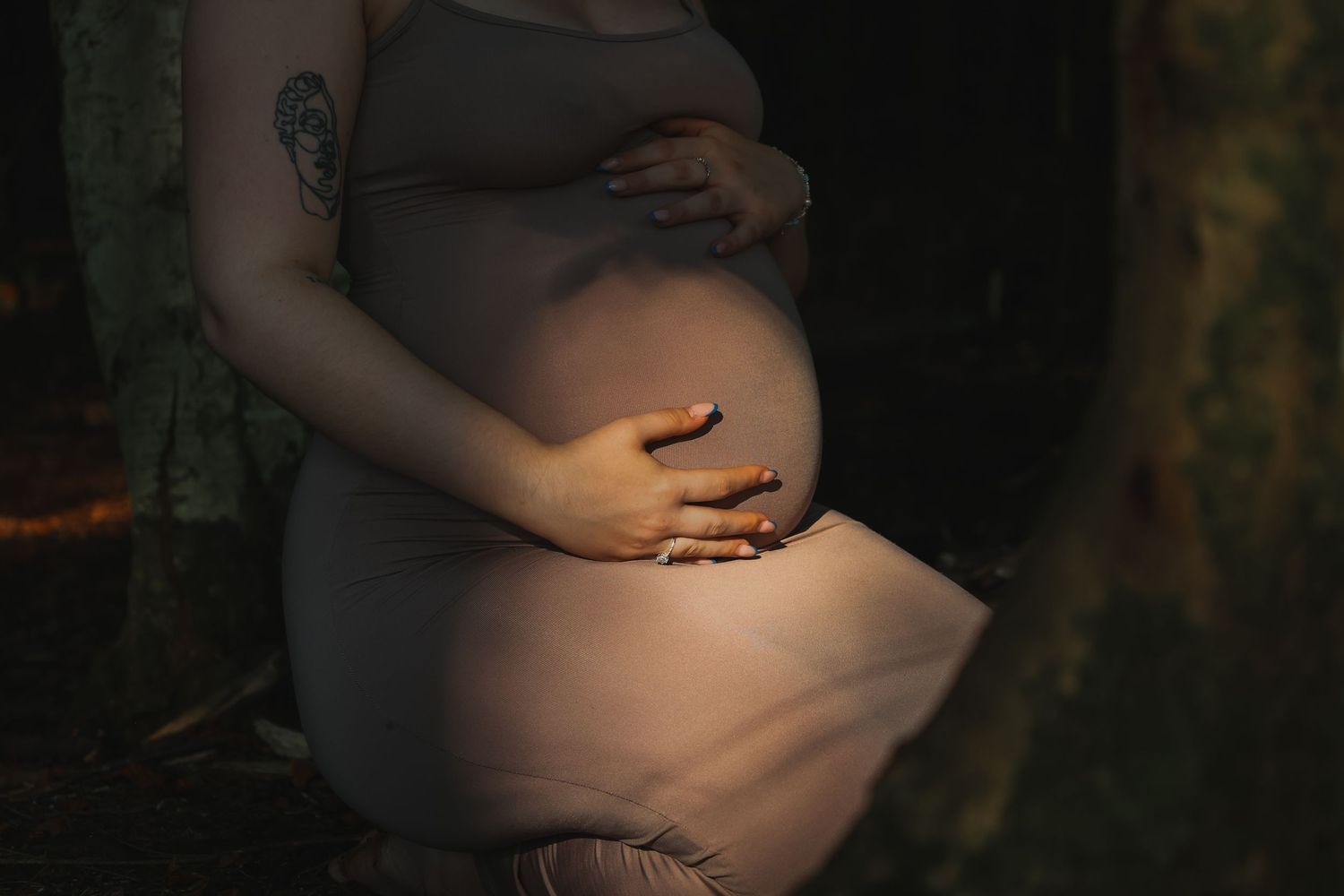 Artistic maternity photo with sunlit pregnant belly against dark background.