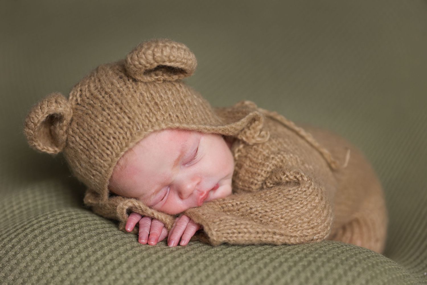 Sleeping newborn in knit bear outfit during professional photo session.
