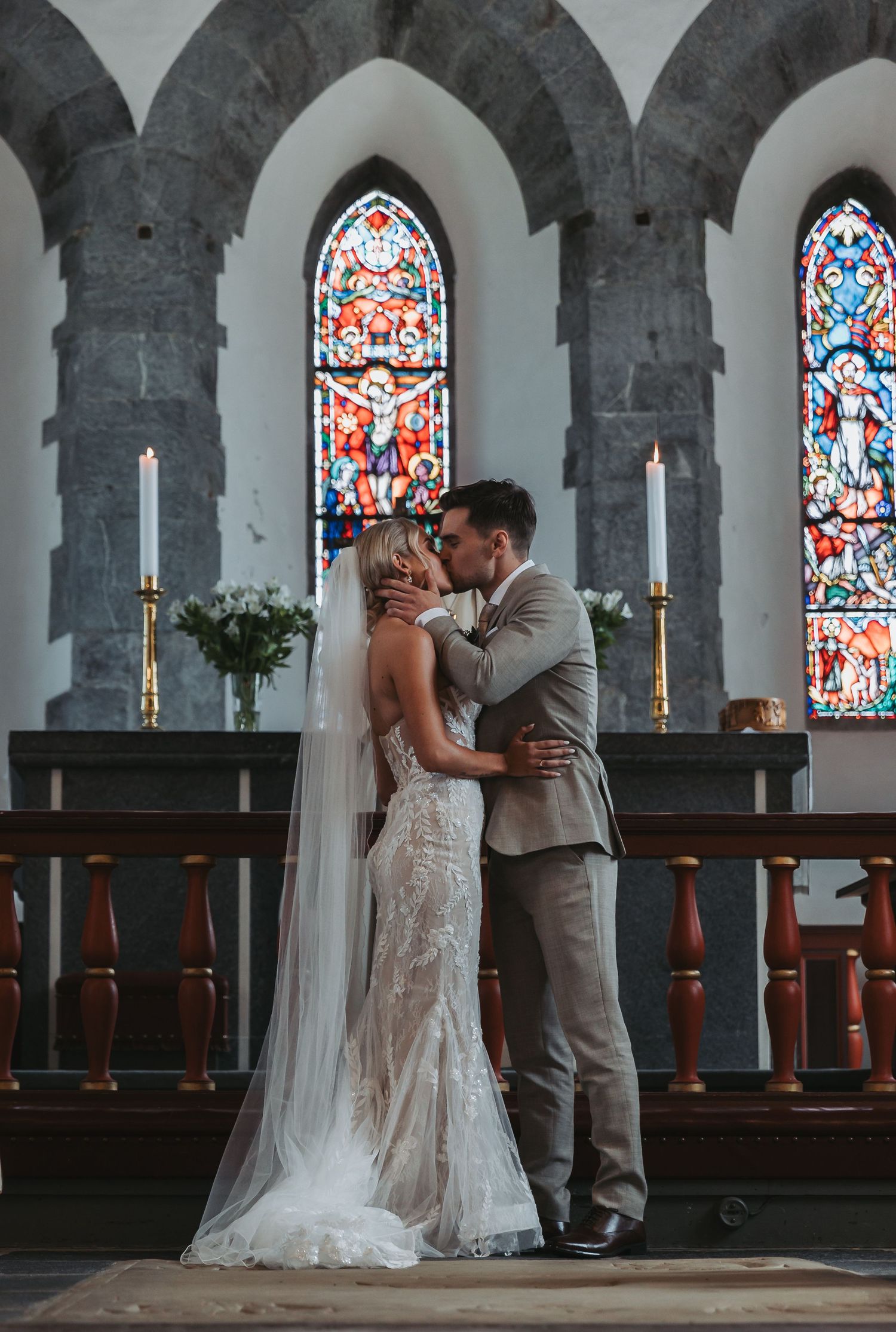 A bride and groom share their first kiss at the altar of a historic church with stunning stained glass windows.