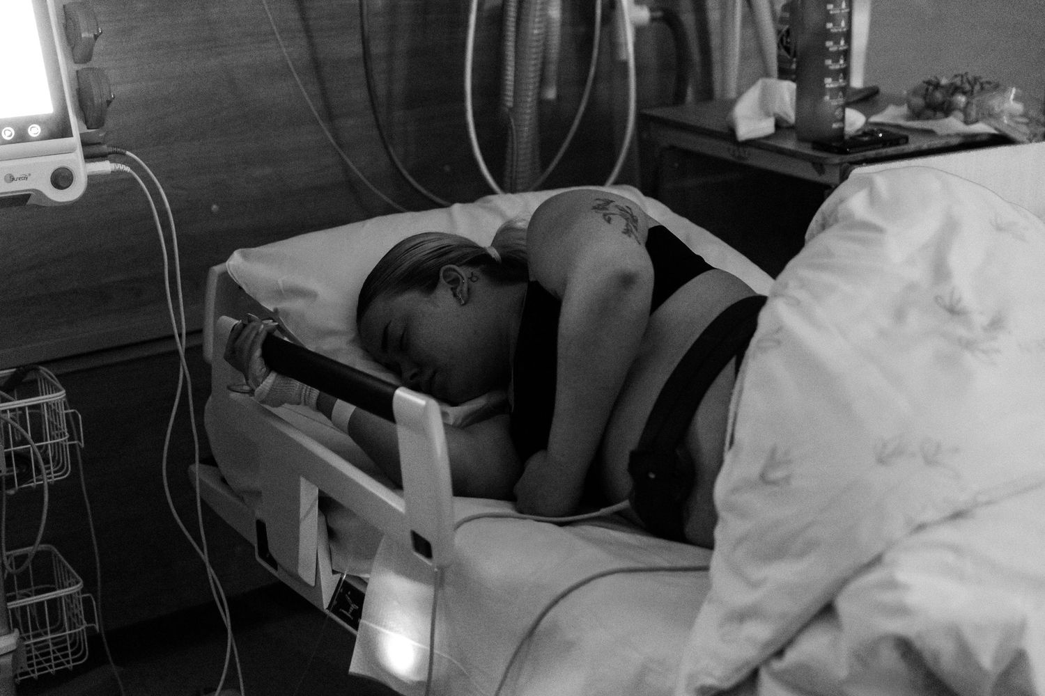 A person rests on a medical bed in a monochrome photo with medical equipment visible in the background.