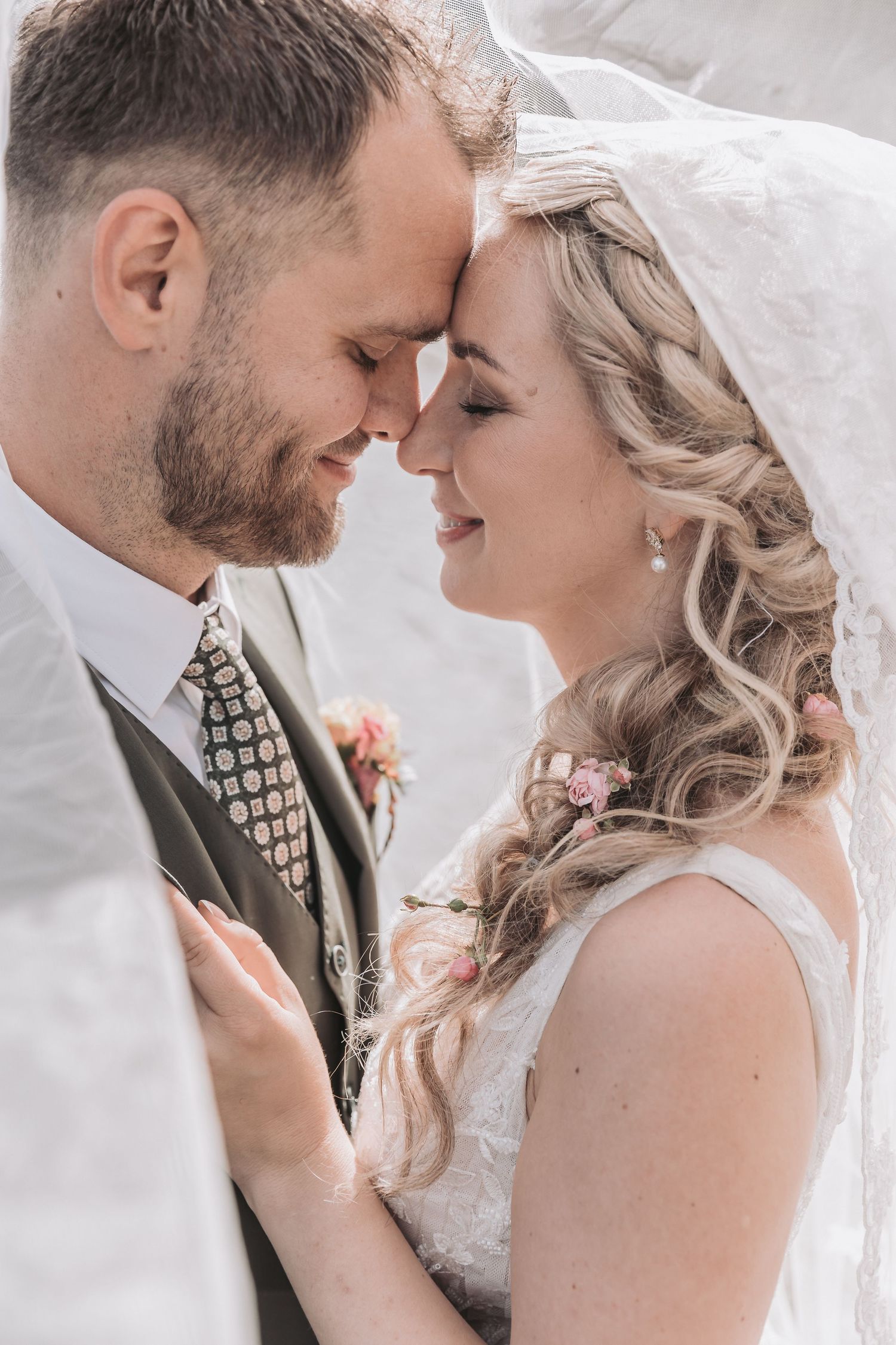 A bride and groom share an intimate forehead touch under a flowing veil on their wedding day.