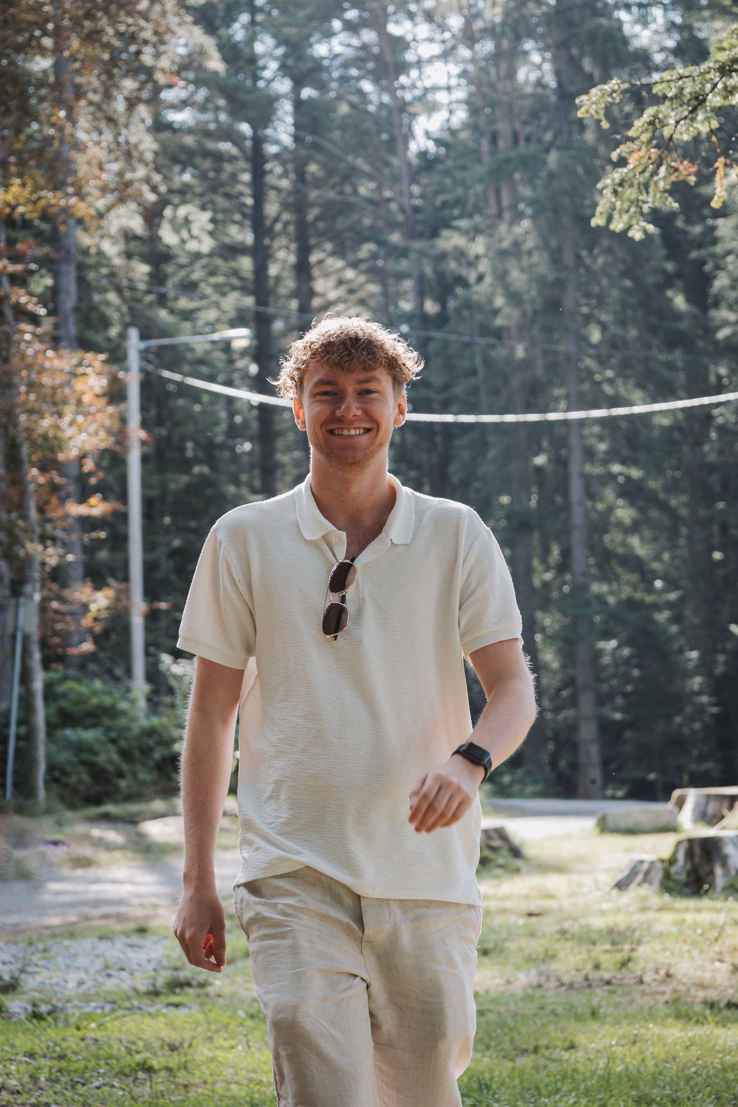 Casual summer portrait in a forest clearing with someone wearing a white polo shirt and khaki shorts.