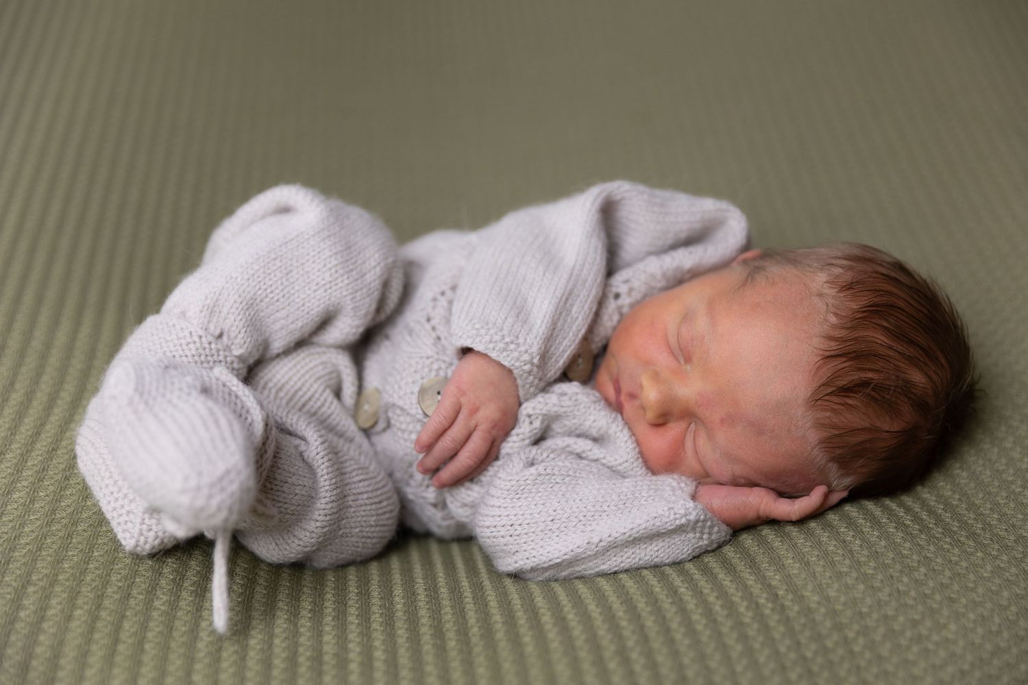Newborn in soft white knitted outfit sleeping peacefully on green fabric.